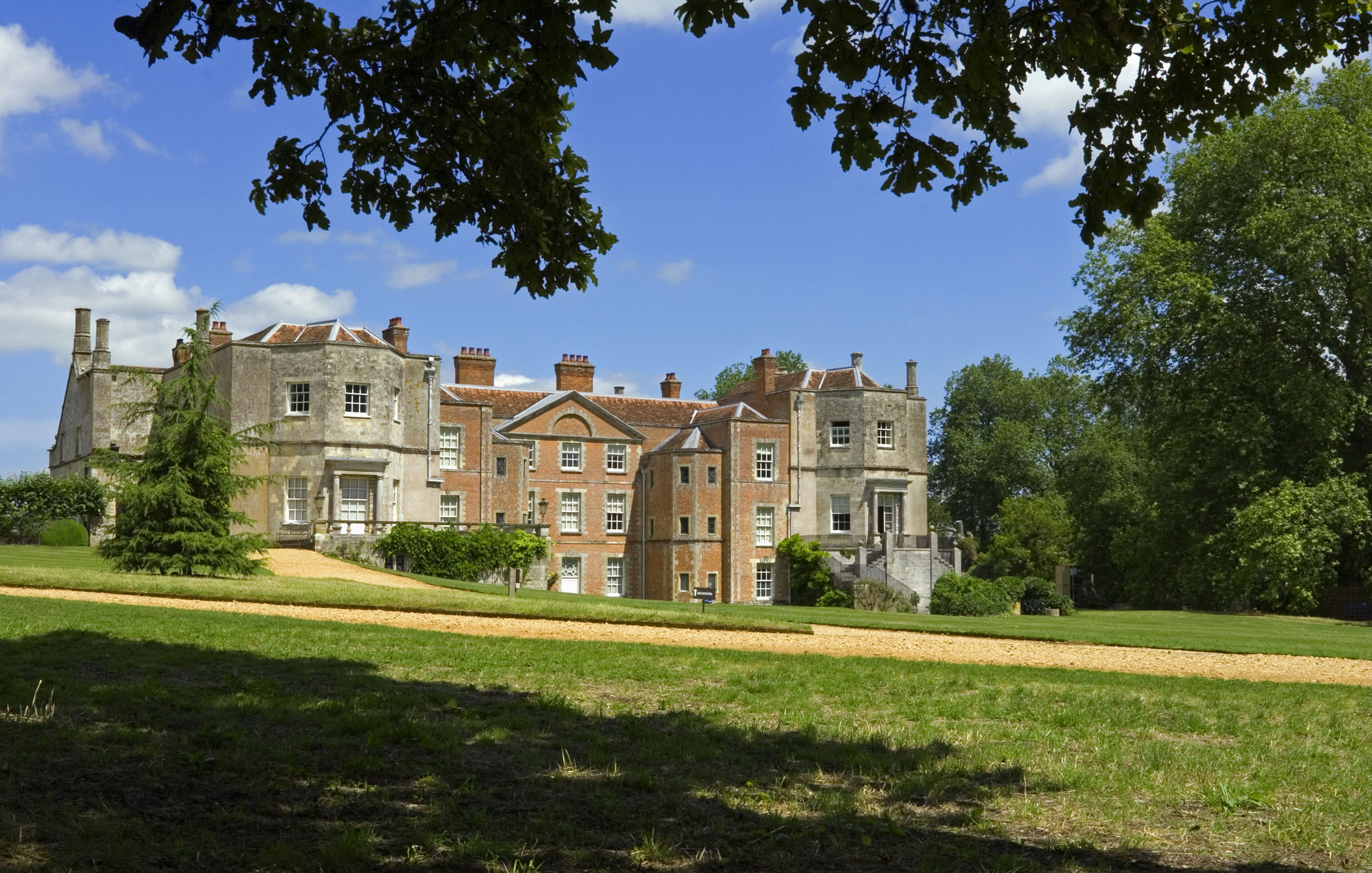 A large three storey country house built of stone and brick, viewed from its grounds. Image ID: B8YXW5.