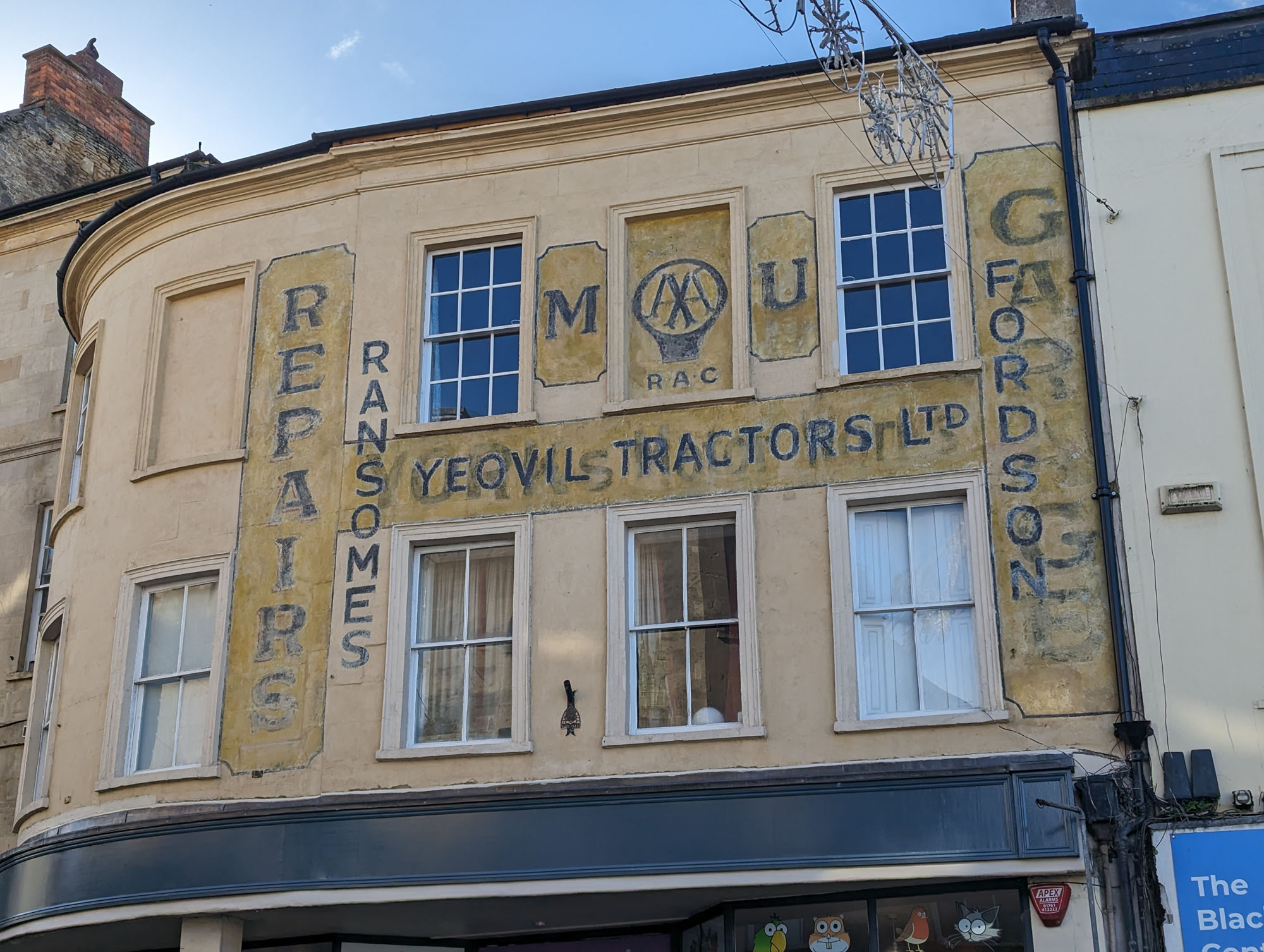 Ghost signs on the first floor of a building with cream walls and multiple sash windows