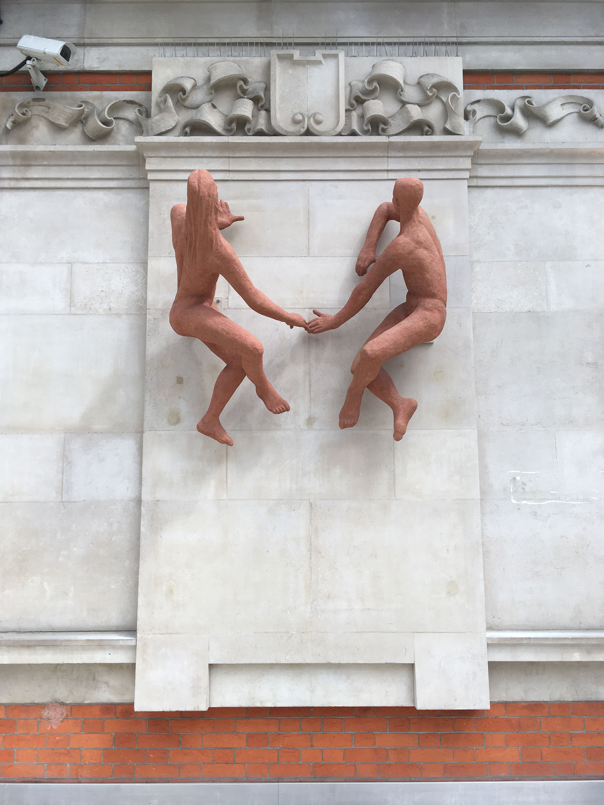Terracotta sculpture of a male and female figure fixed to a marble clad wall in London Waterloo station.
