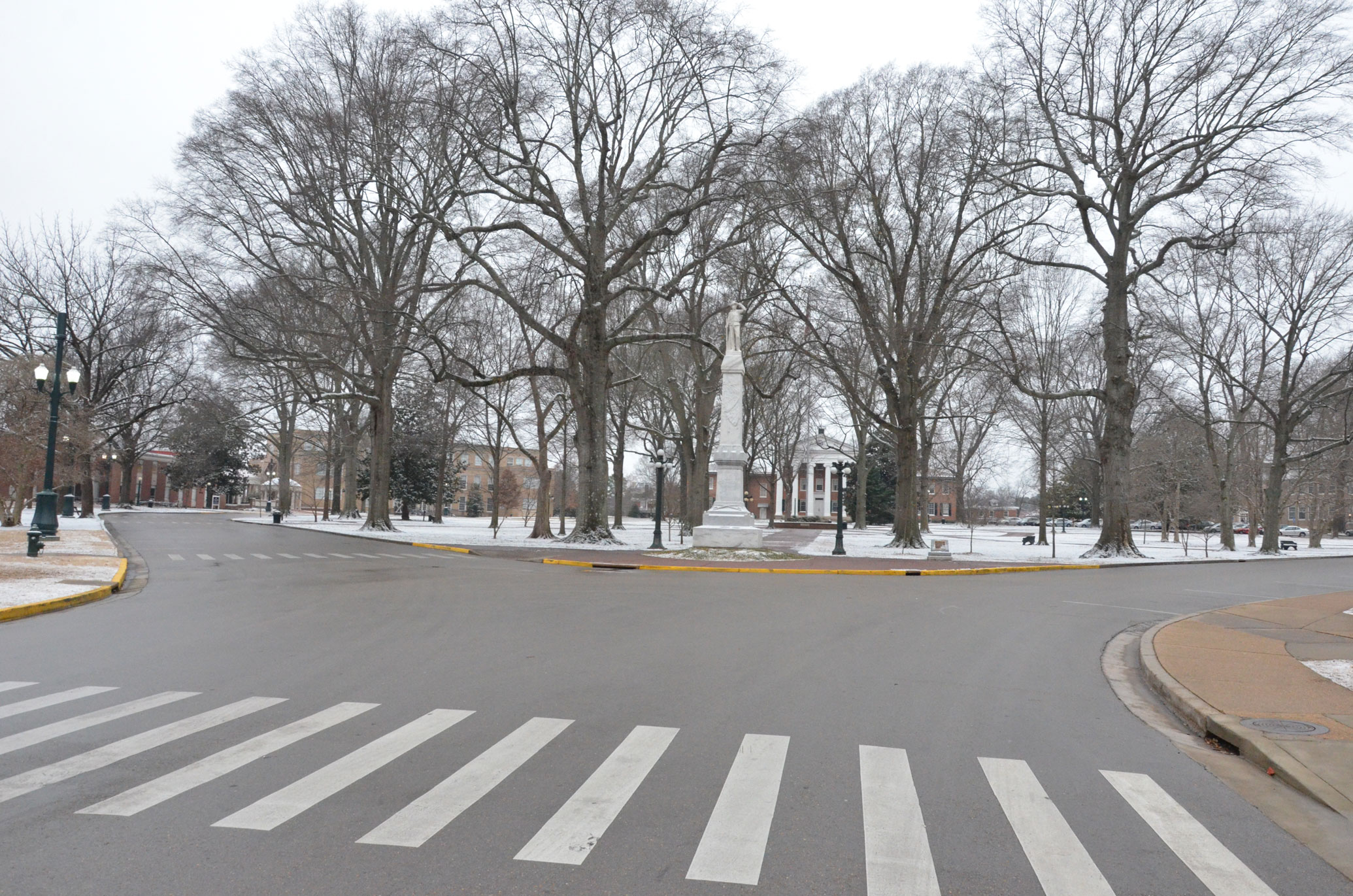 View of the original location of a confederate monument comprising a military statue atop a tall column, with university buildings in the background.
