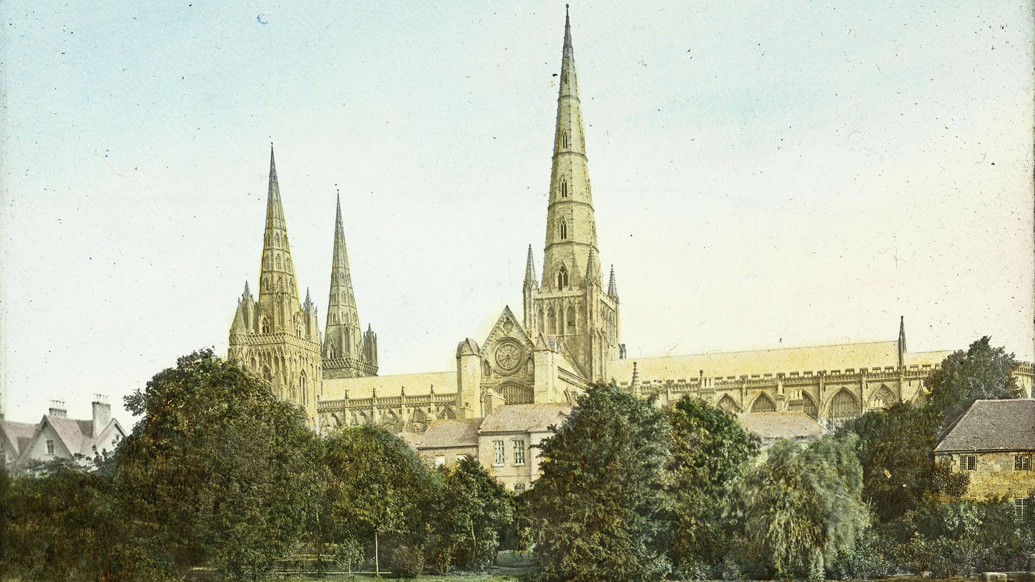 Arcive coloured photo of a Cathedral with a spire behind trees.