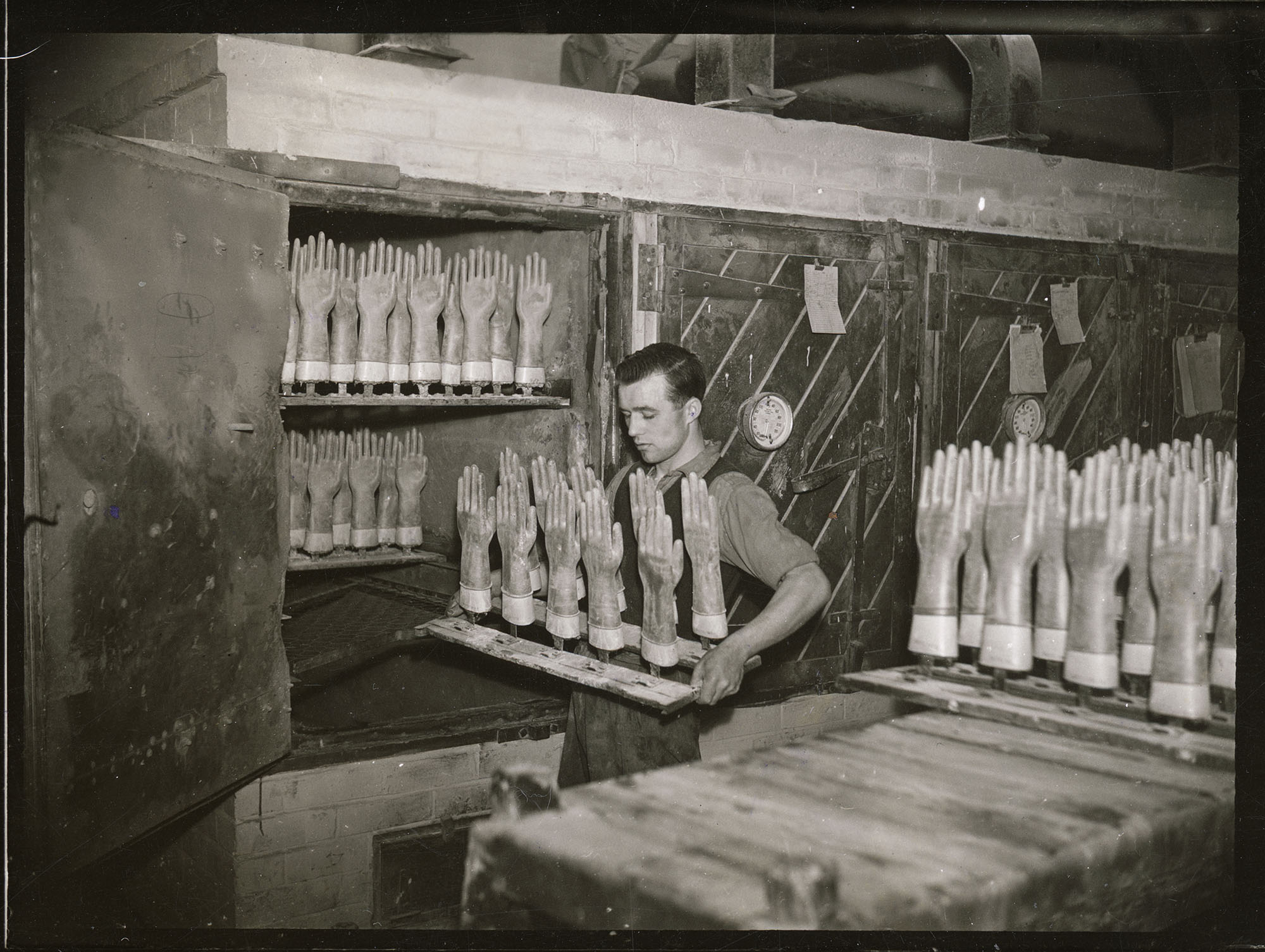 A man placing rubber gloves on moulds into an oven in a factory producing rubber gloves