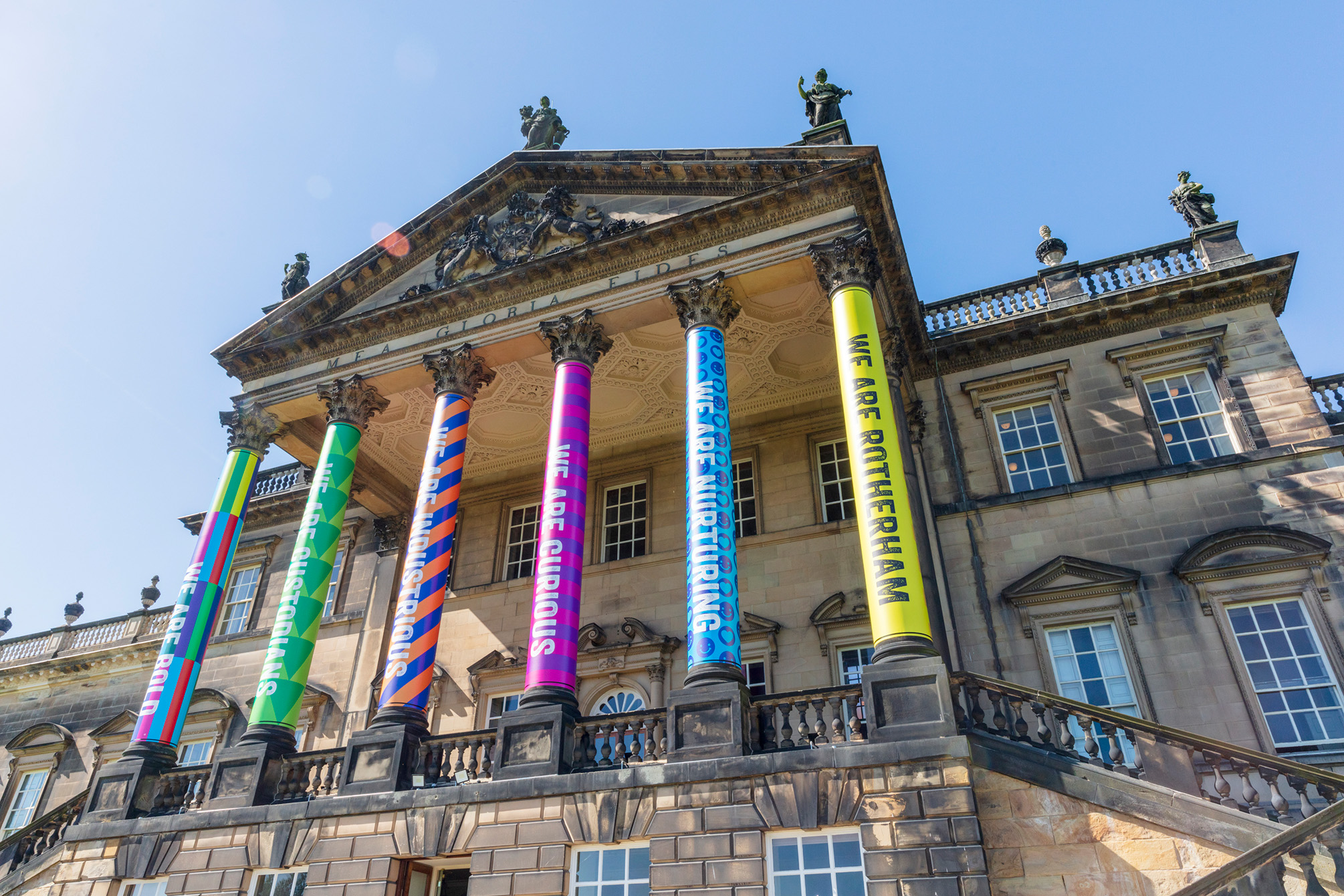 Exterior view of the portico to Wentworth Woodhouse with its pillars decorated with colourful slogan-bearing wraps.
