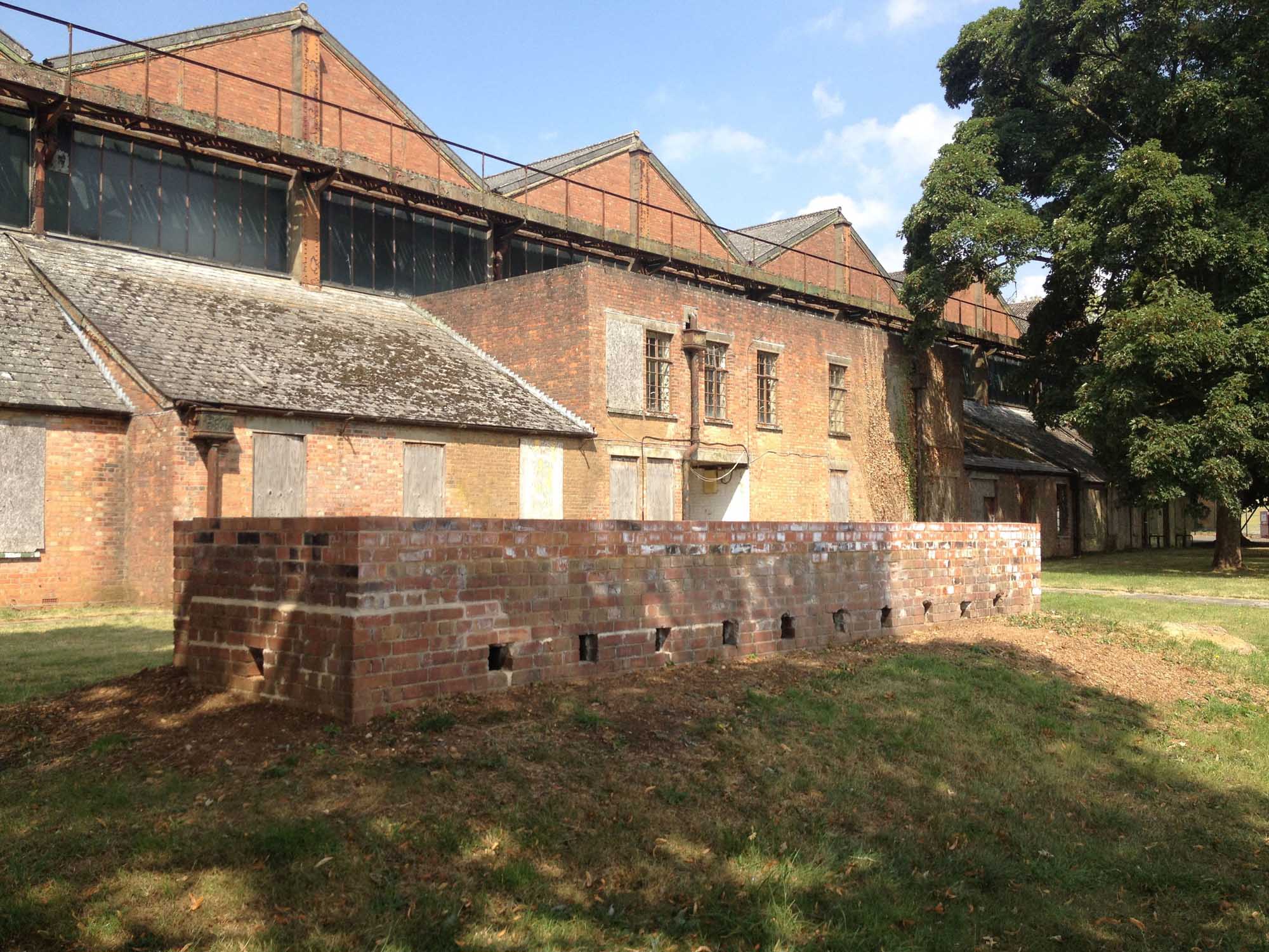 Brick buildings at RAF Bicester with grass, trees and brick structure in foreground.
