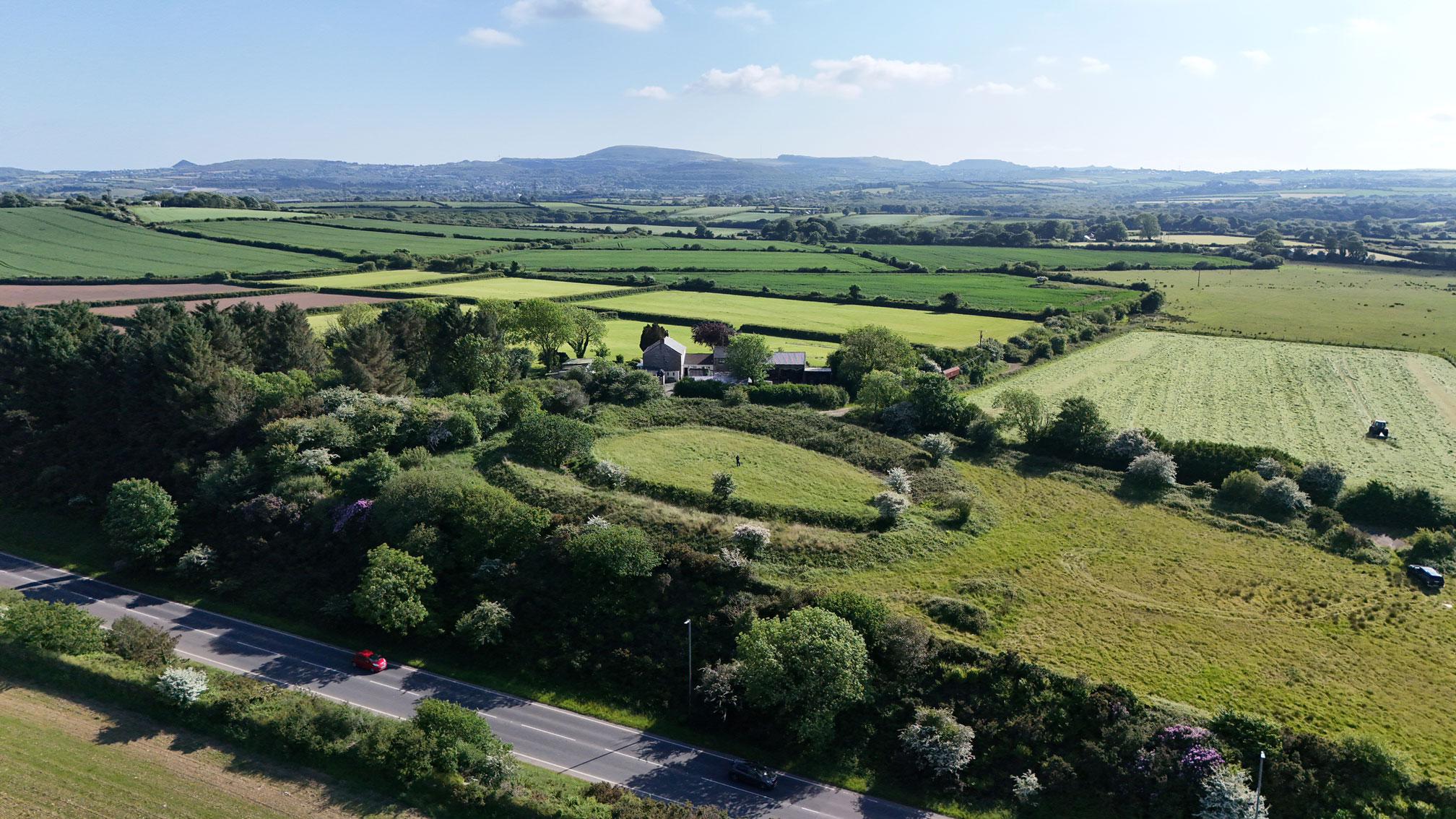 An aerial view of the earthworks of a henge next to a road.