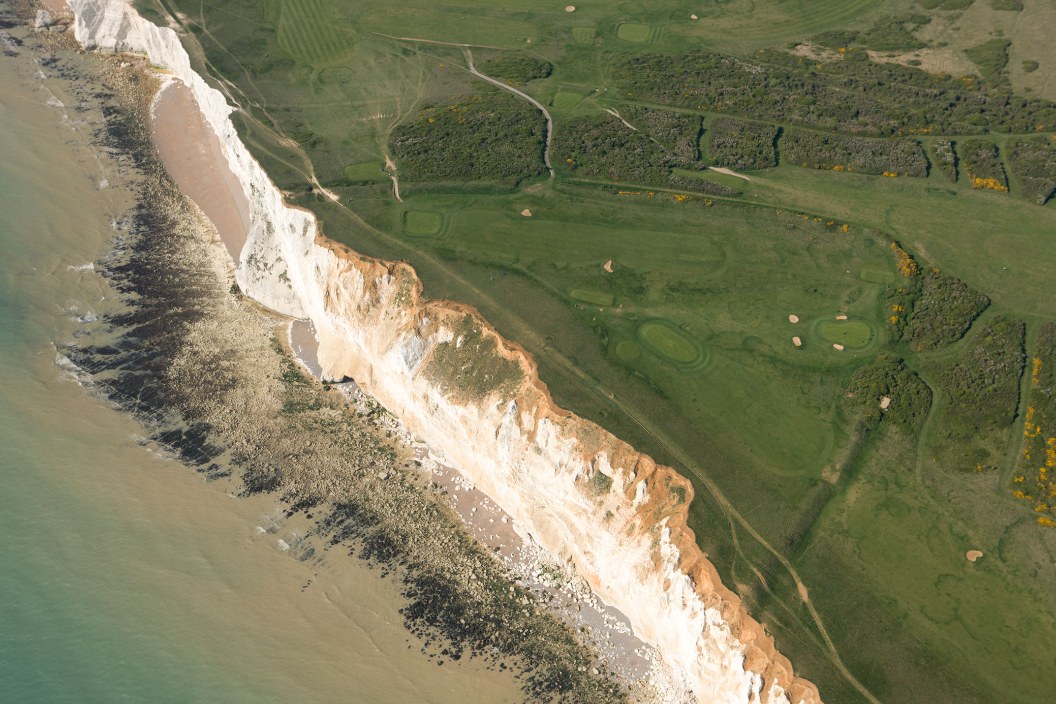 An aerial view of the earthworks of a coastal hillfort situated in close proximity to an eroding cliff.