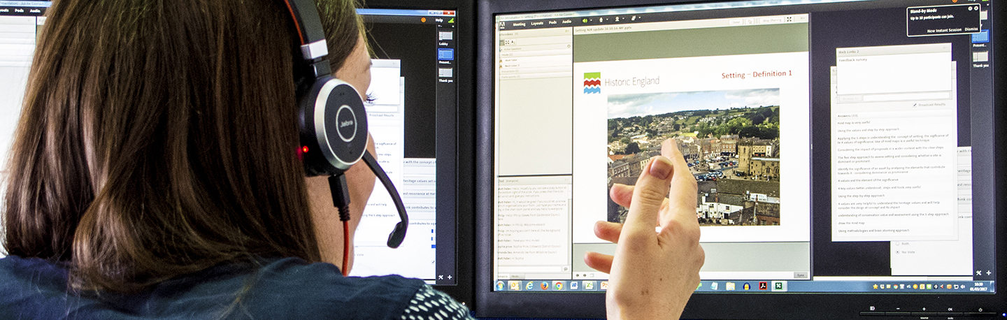 Woman wearing headset and microphone pointing at a computer screen