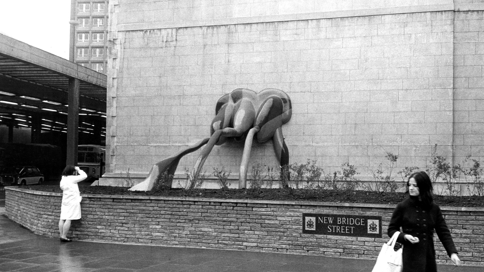 Fibreglass sculpture spilling out from an external wall into a flower-bed
