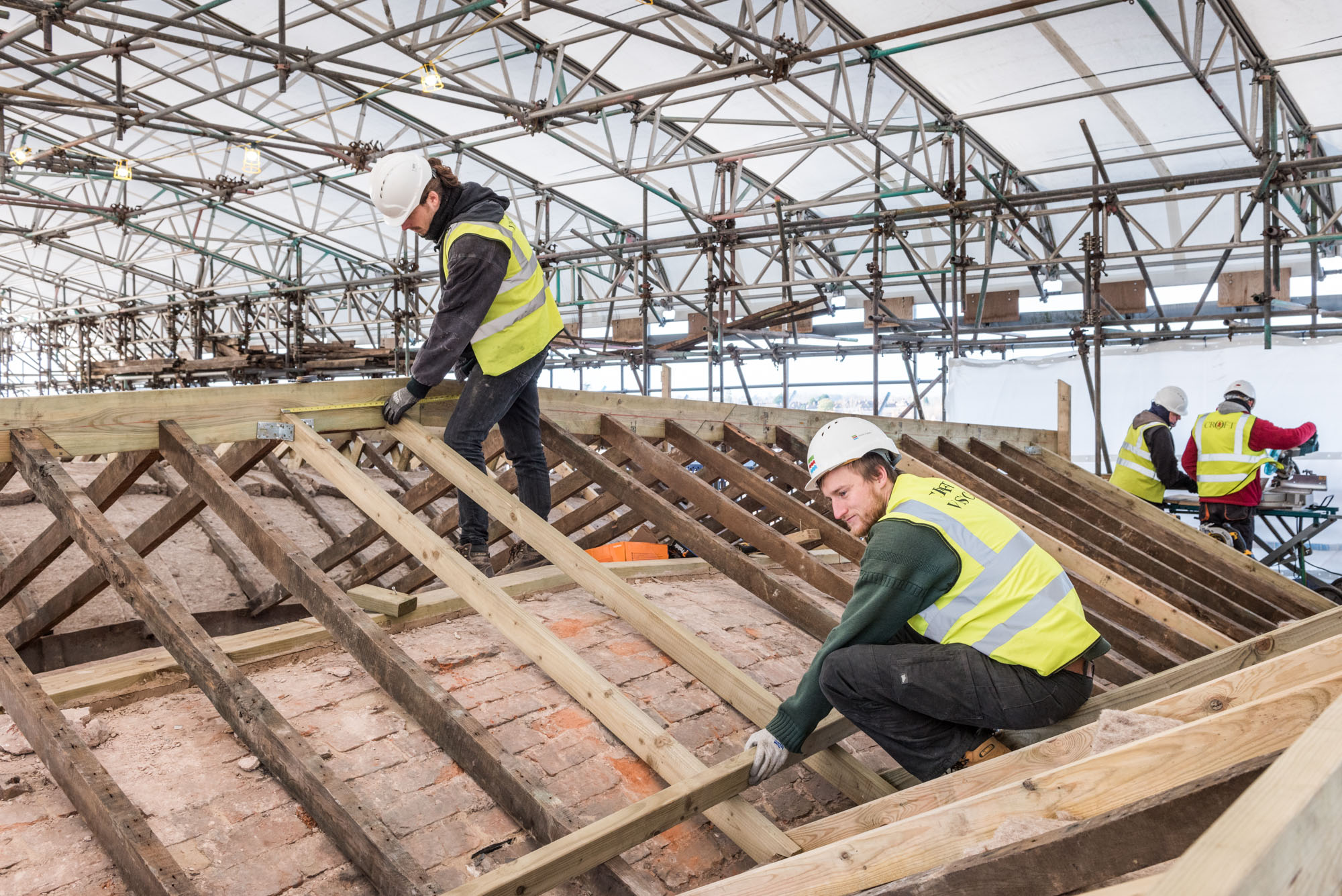Two men in hard hats and high viz jackets repairing roof under scaffolding