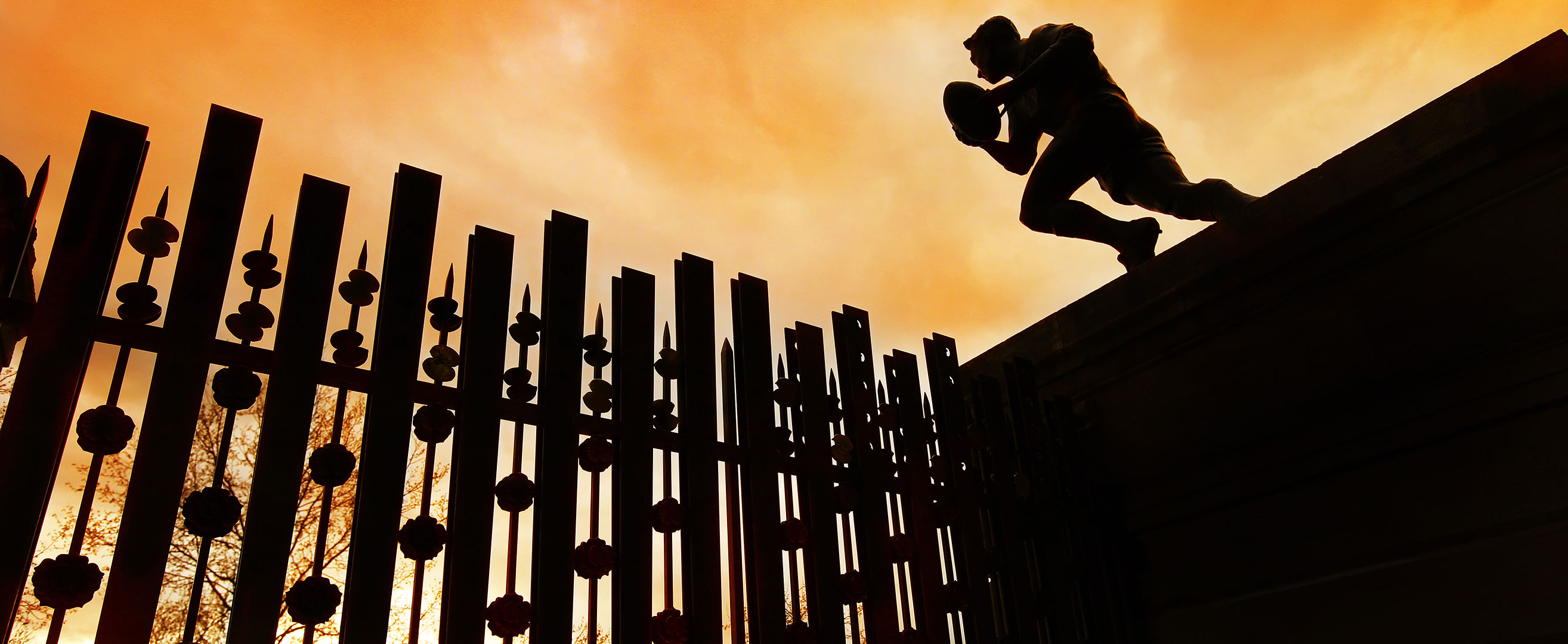 Silhouette of statue of rugby player situated above gates