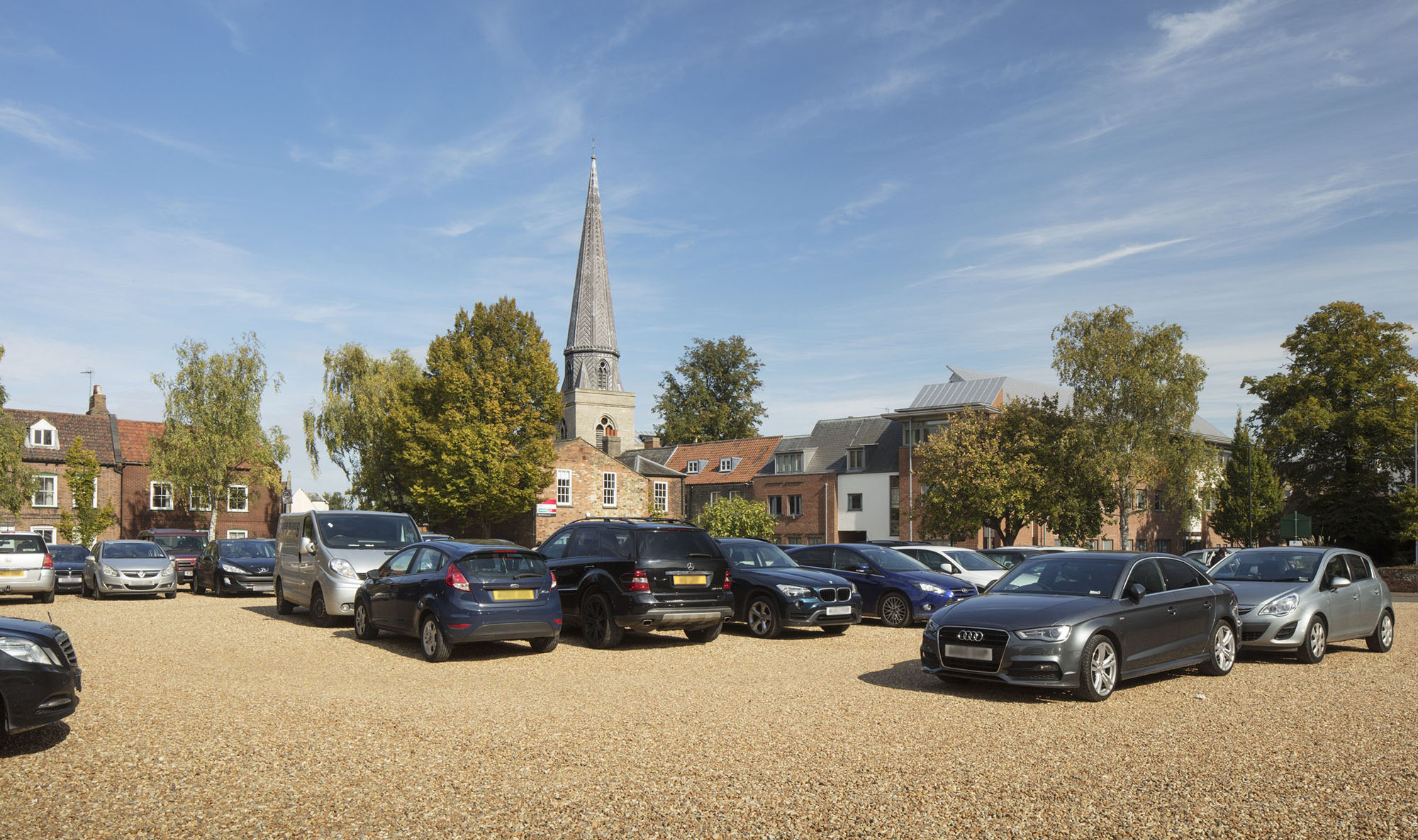 Cars parked in car park with church spire in background