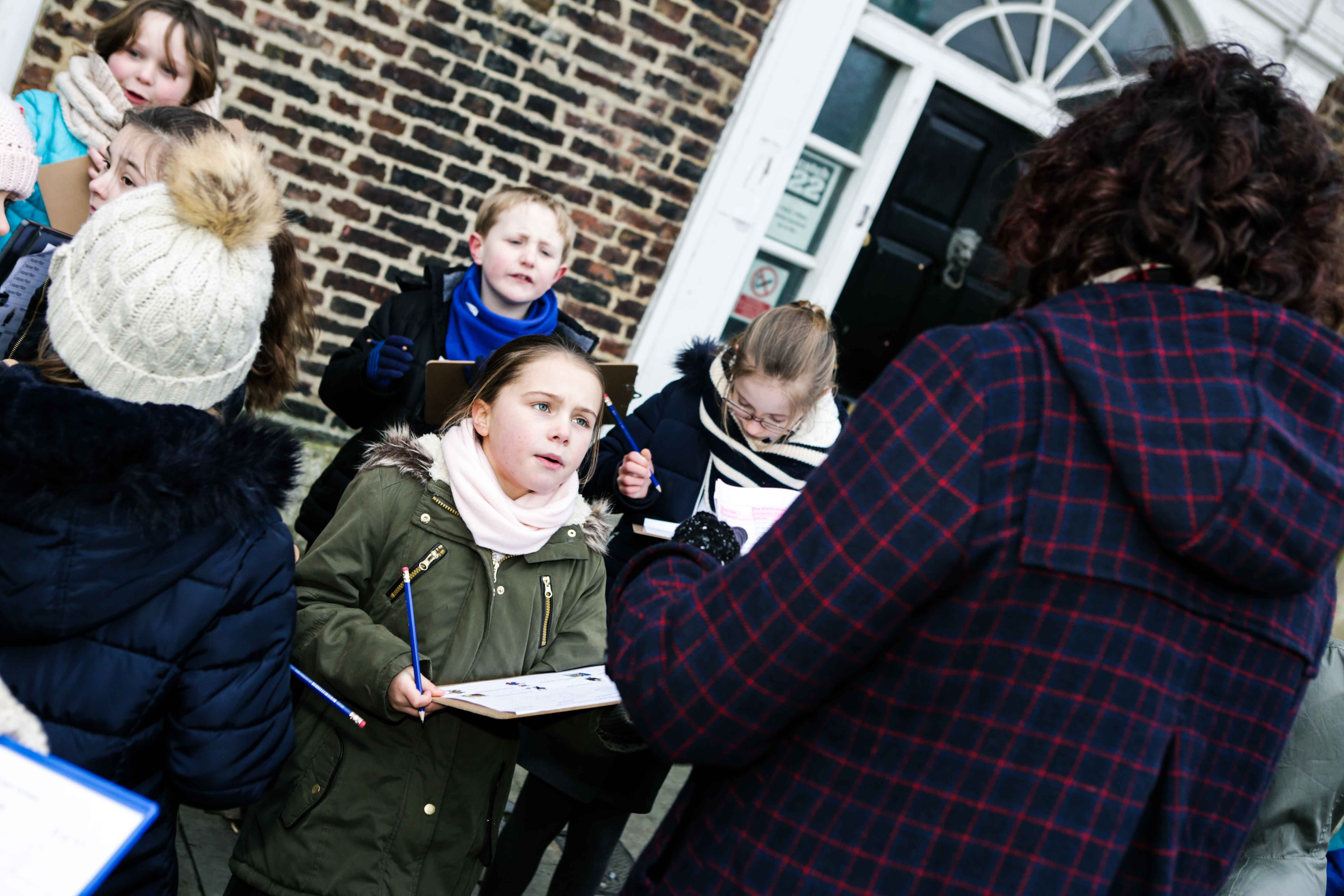 Children cluster around a teacher with clipboards.