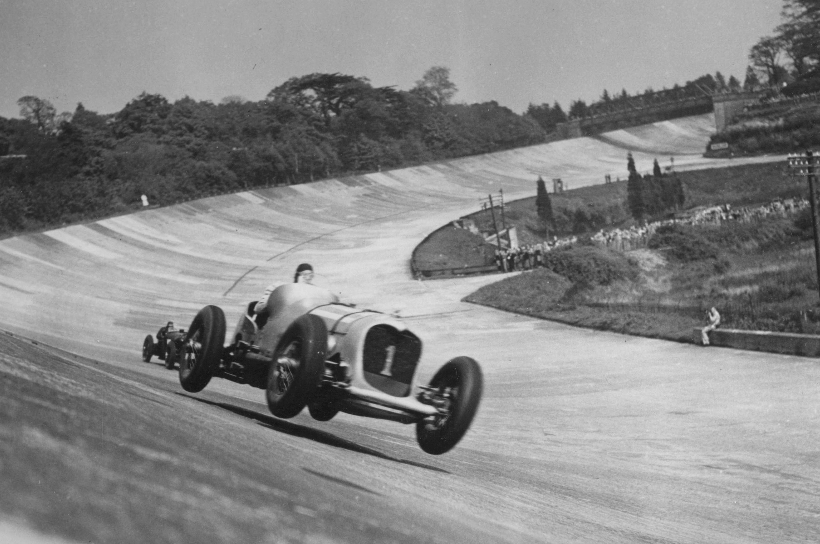 Black and white image of a car lifted off the track at Brooklands as it takes a fast corner.