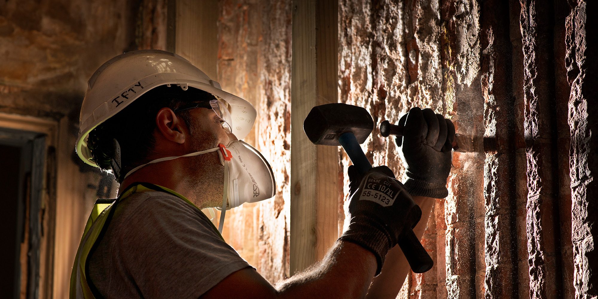 A mason in PPE works stone in low light. 