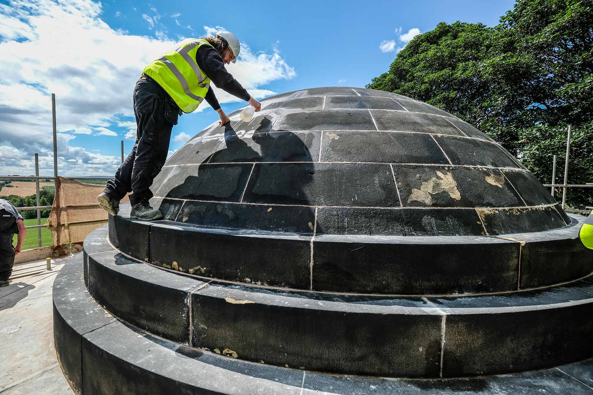 A person standing on a domed roof spraying a liquid onto it.