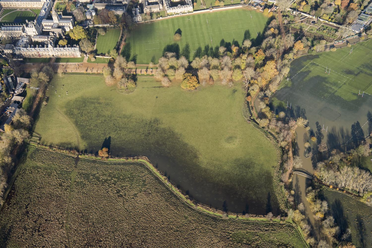 An aerial view of a meadow with a flooded river to the right.