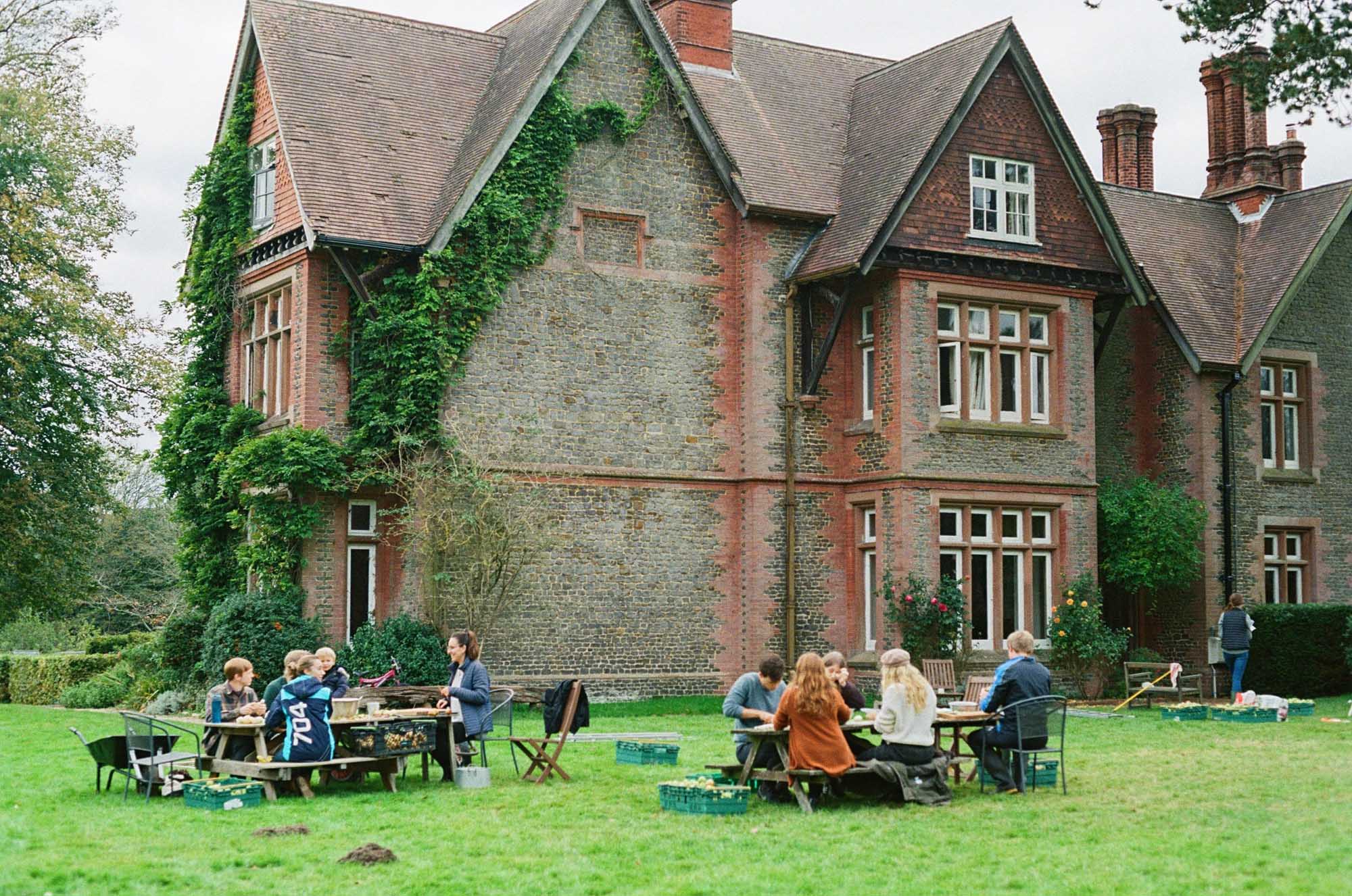 People sat on picnic benches outside a historic house.