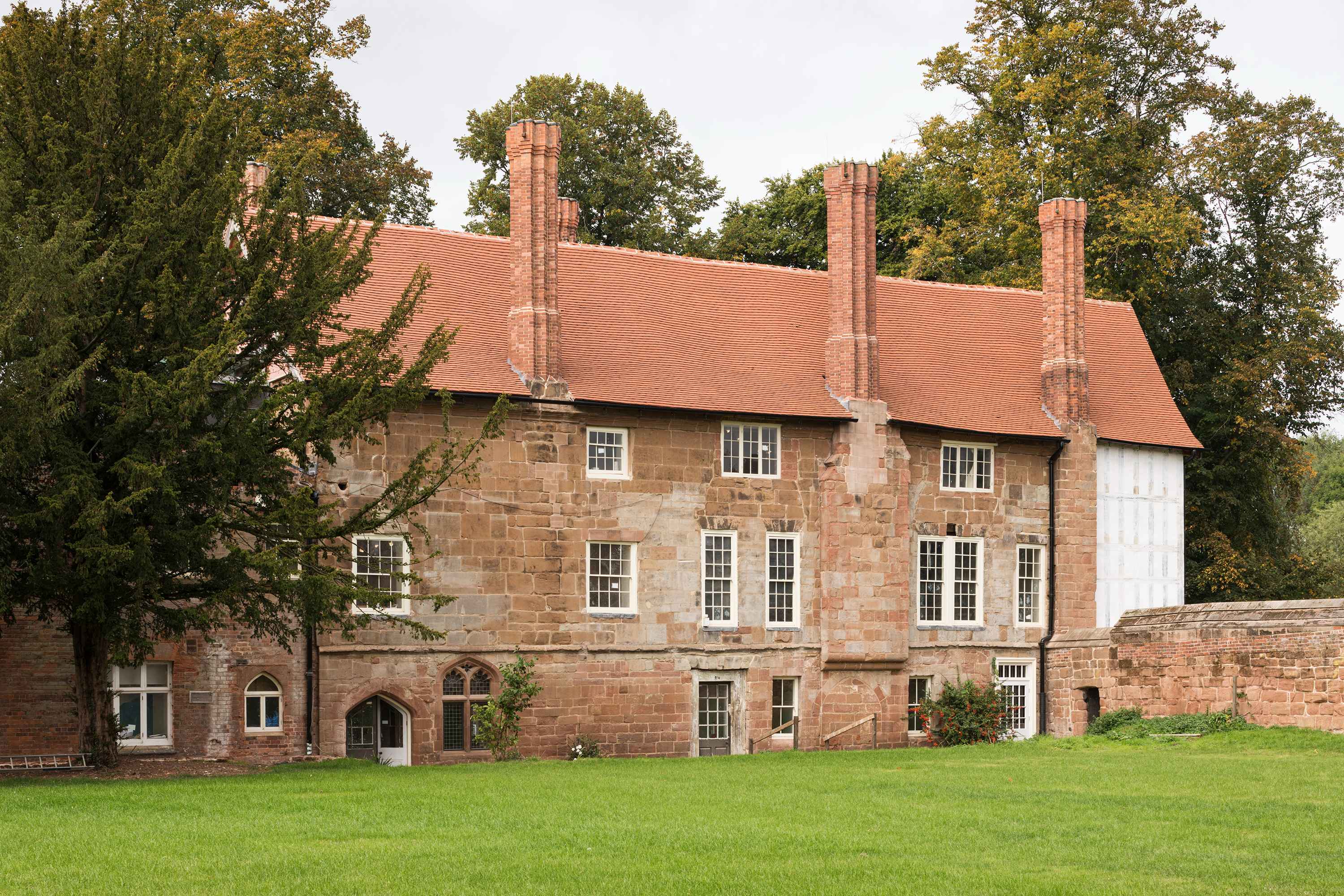 A large three-storey stone house with multiple chimneys and a timbered end section. 