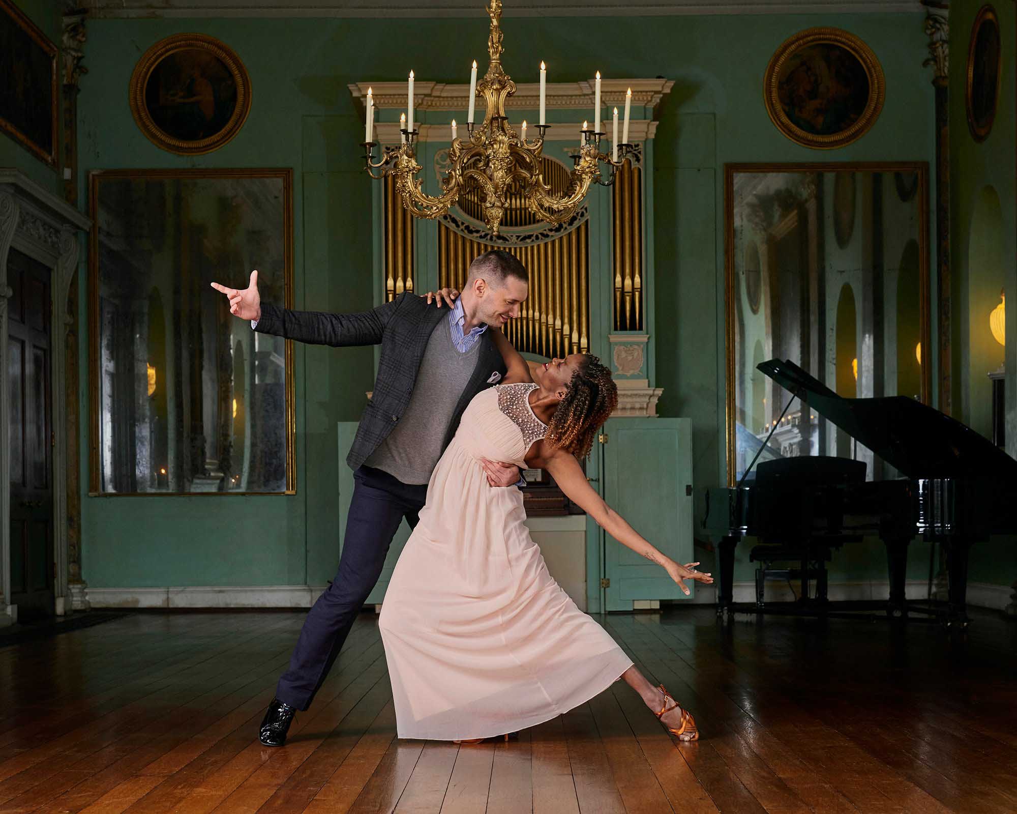 A couple dancing under a chandelier and a piano and organ in the background