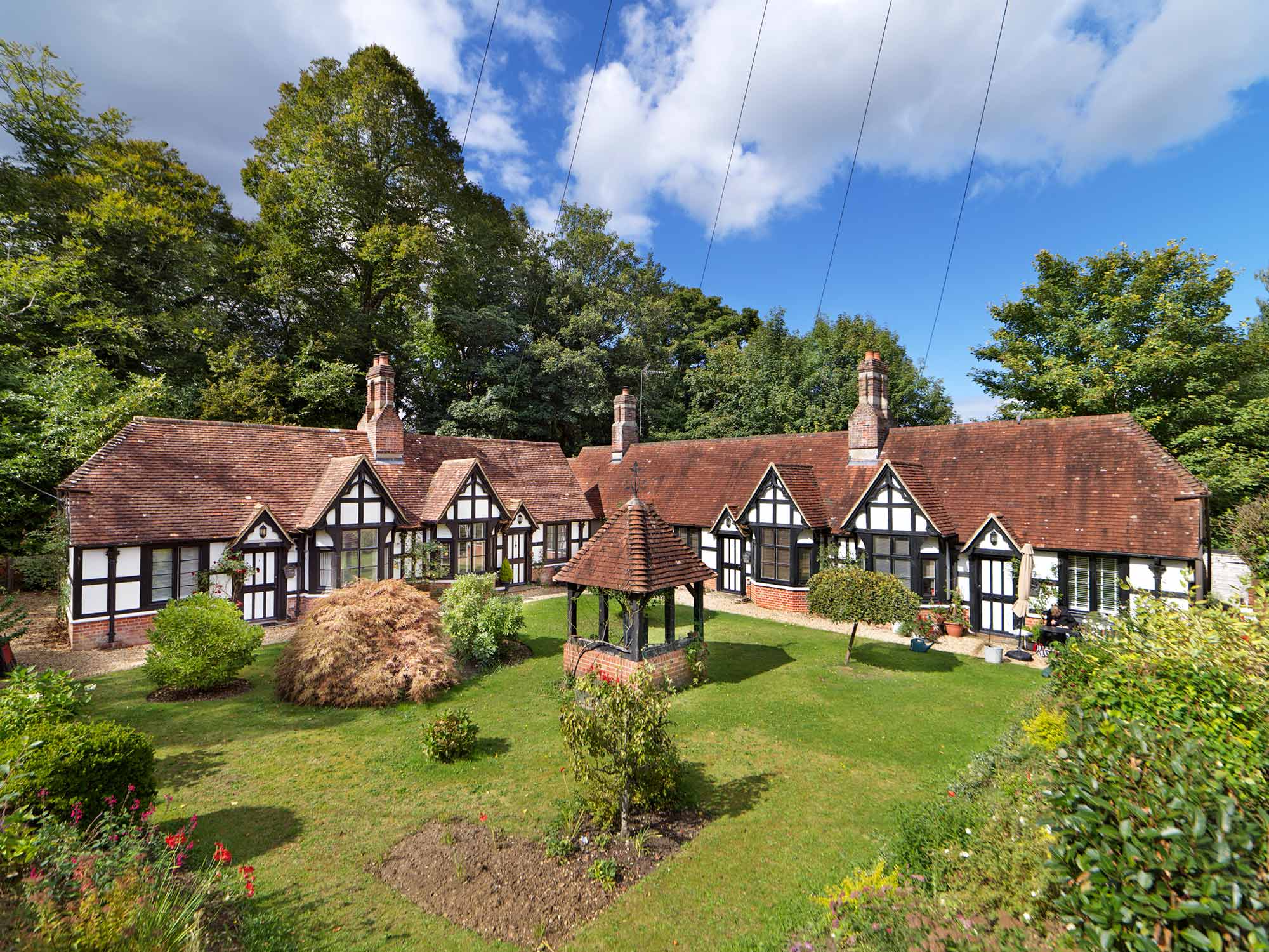 General view of the almshouses and their front green with central well from the south-east.