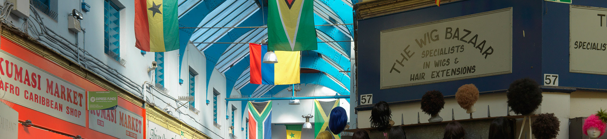 Upward-angle photograph of the interior of a market hall, showing the names of shop fronts and international flags hanging from the rafters.