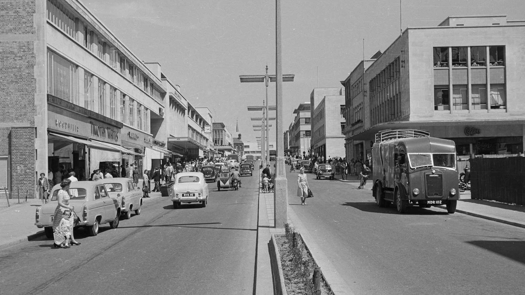 archive black and white photograph of a busy street scene with people and vehicles