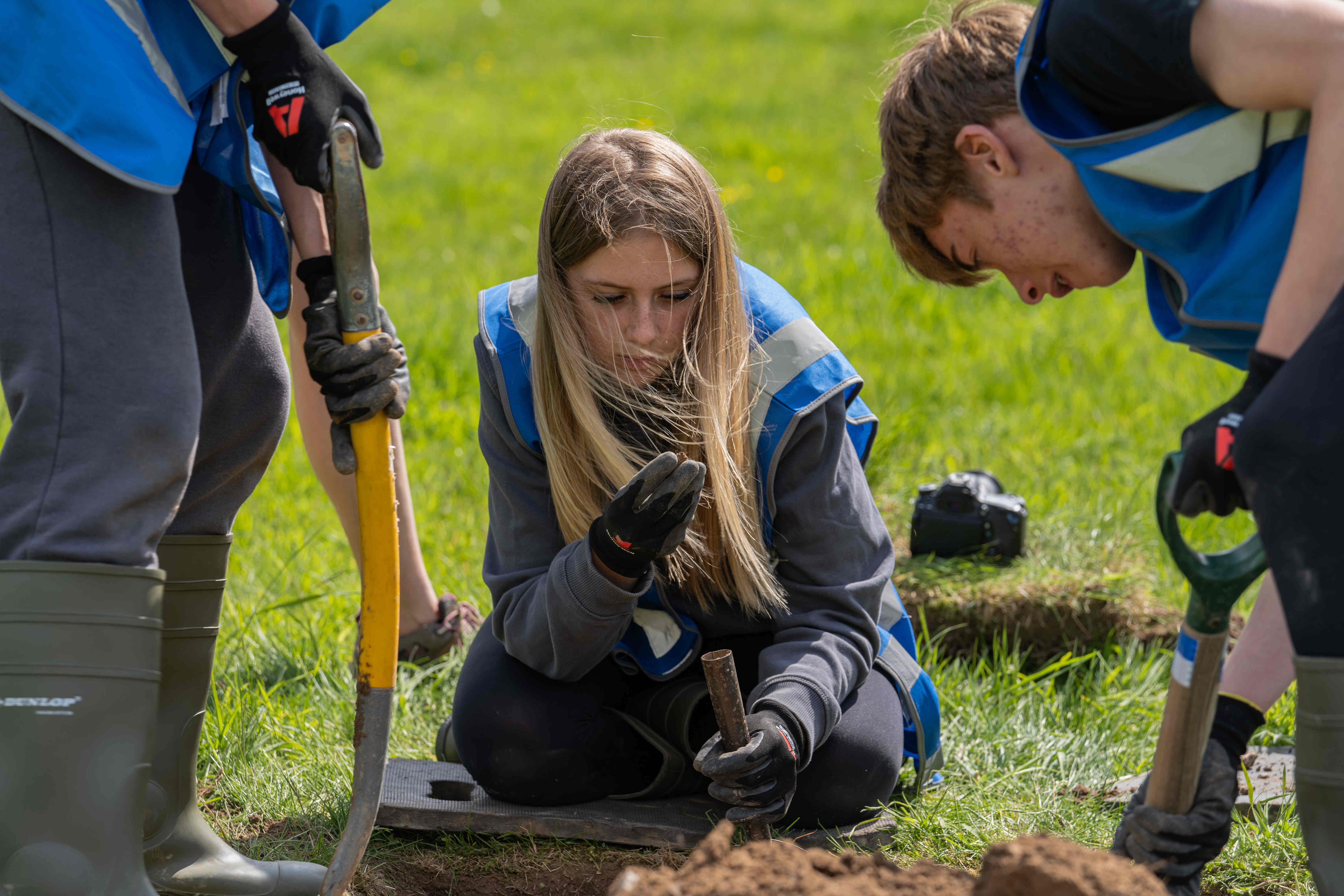 Three people with tools examining an archaeological dig site.