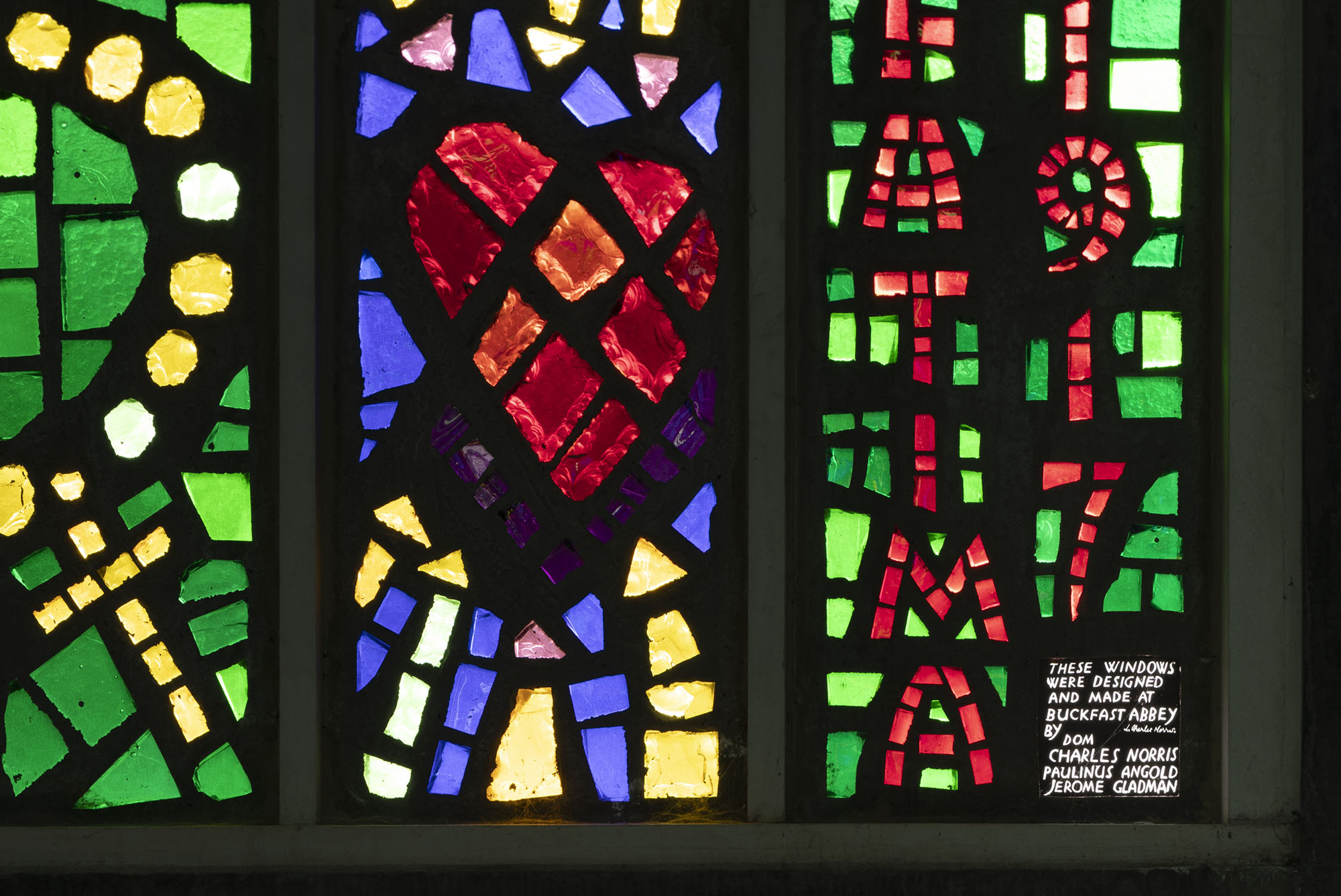 The photo shows three panels of chunky glass design, with vibrant red, green, yellow and blue in a black background, with a heart in the centre panel.