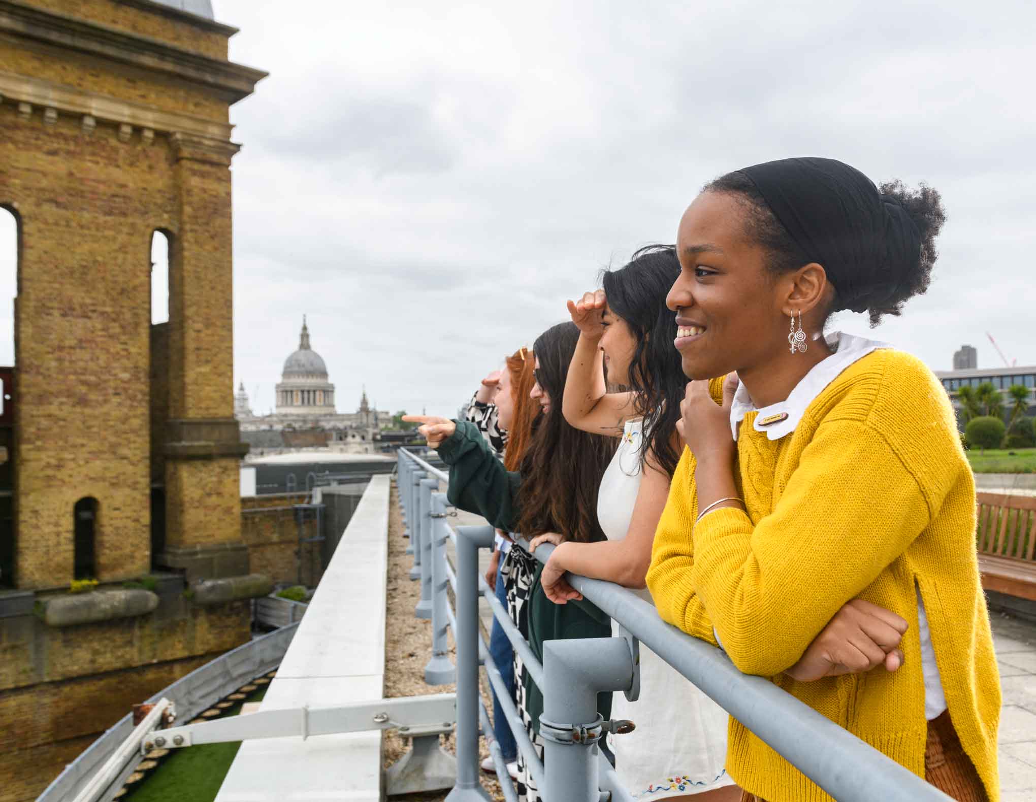 Group of young people looking in the distance towards view of London, whilst leaning on the parapet of Cannon Bridge House roof garden.