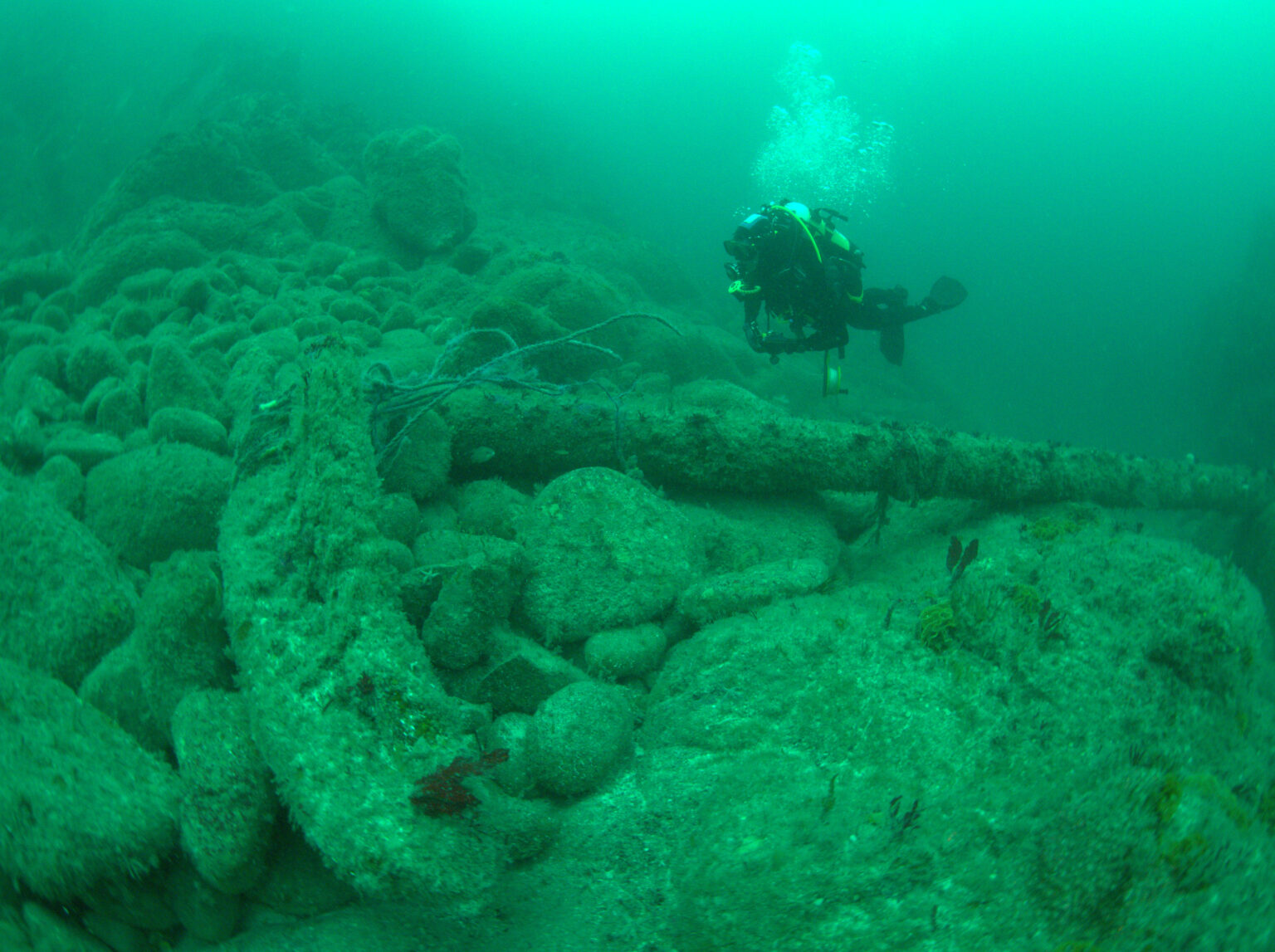 Diver examining a large anchor on the seabed.