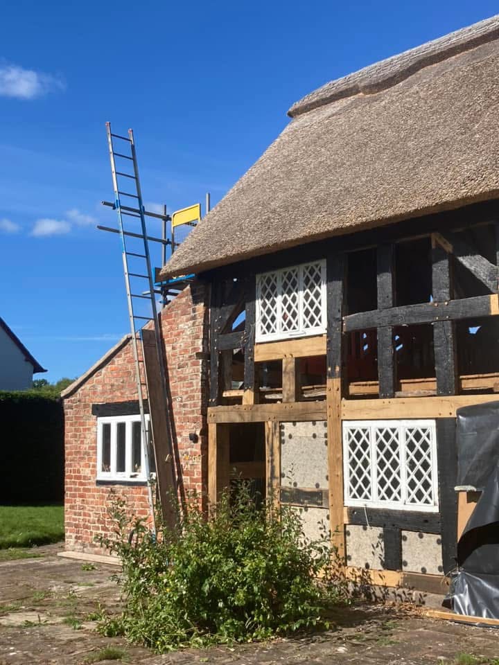 A timber-framed thatched house with infill panels removed to install insulation.