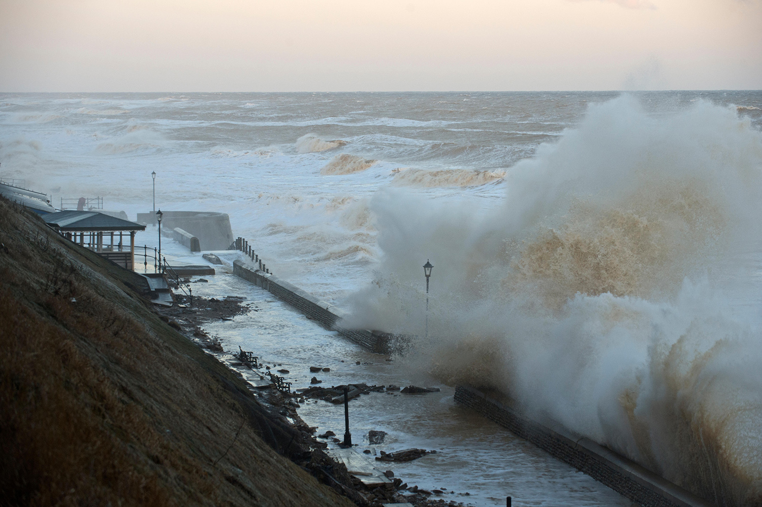 A large wave crashes over a seafront.