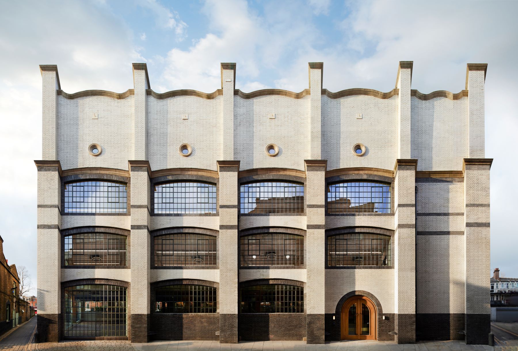 Front view of a white brick building with a wavy roof, large windows and portholes