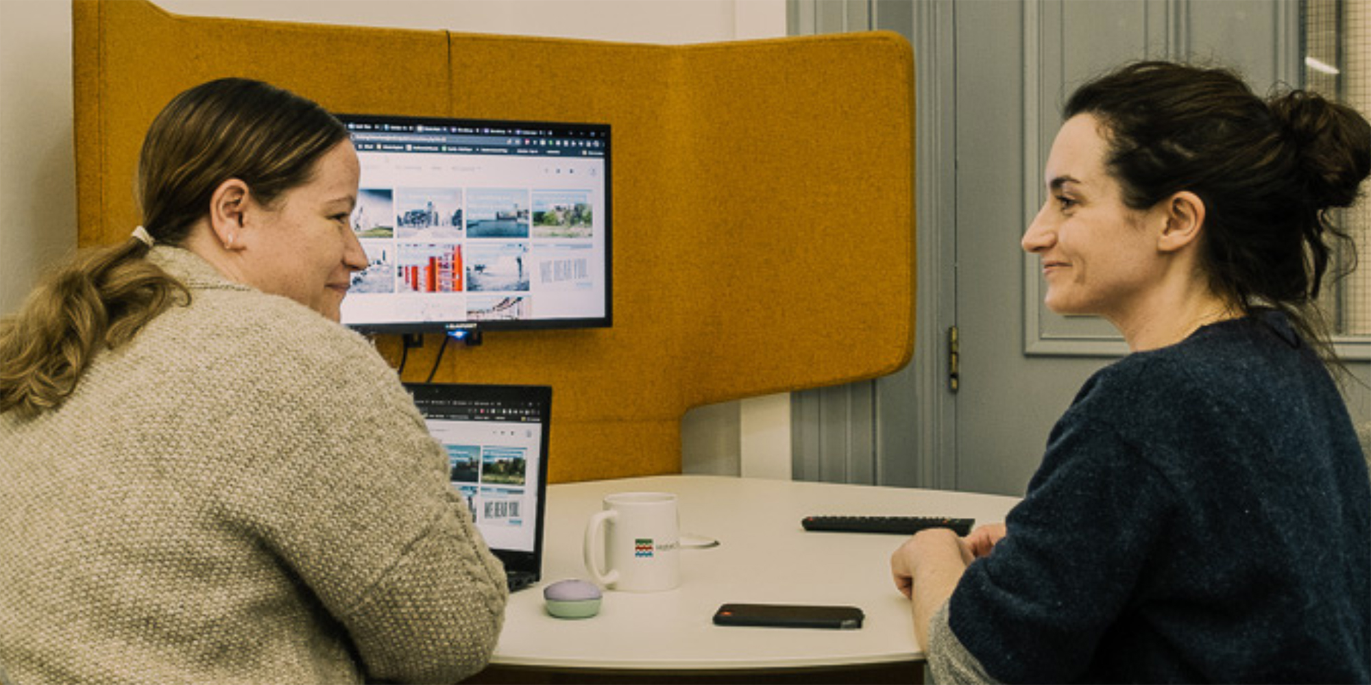 Two women smile while having a meeting at a desk