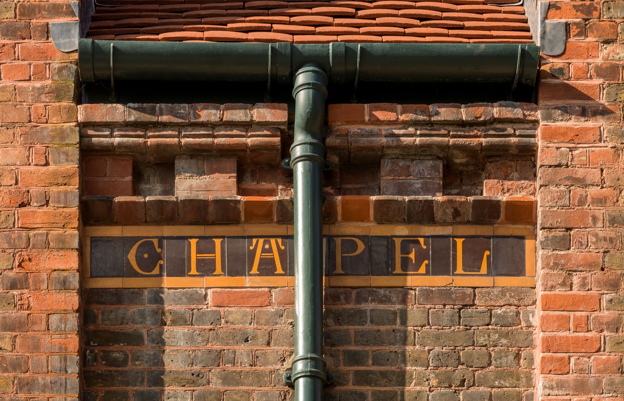 A photograph of red brickwork with decorative lettering on tiles spelling the word chapel.