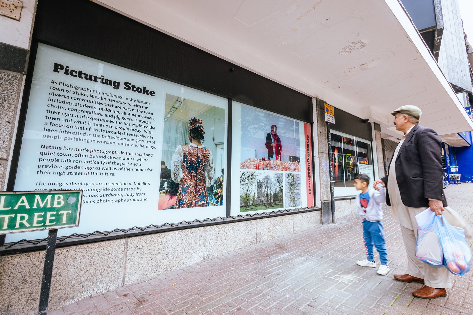 An older man and a young boy look at a high street window displaying "Picturing Stoke" artwork.