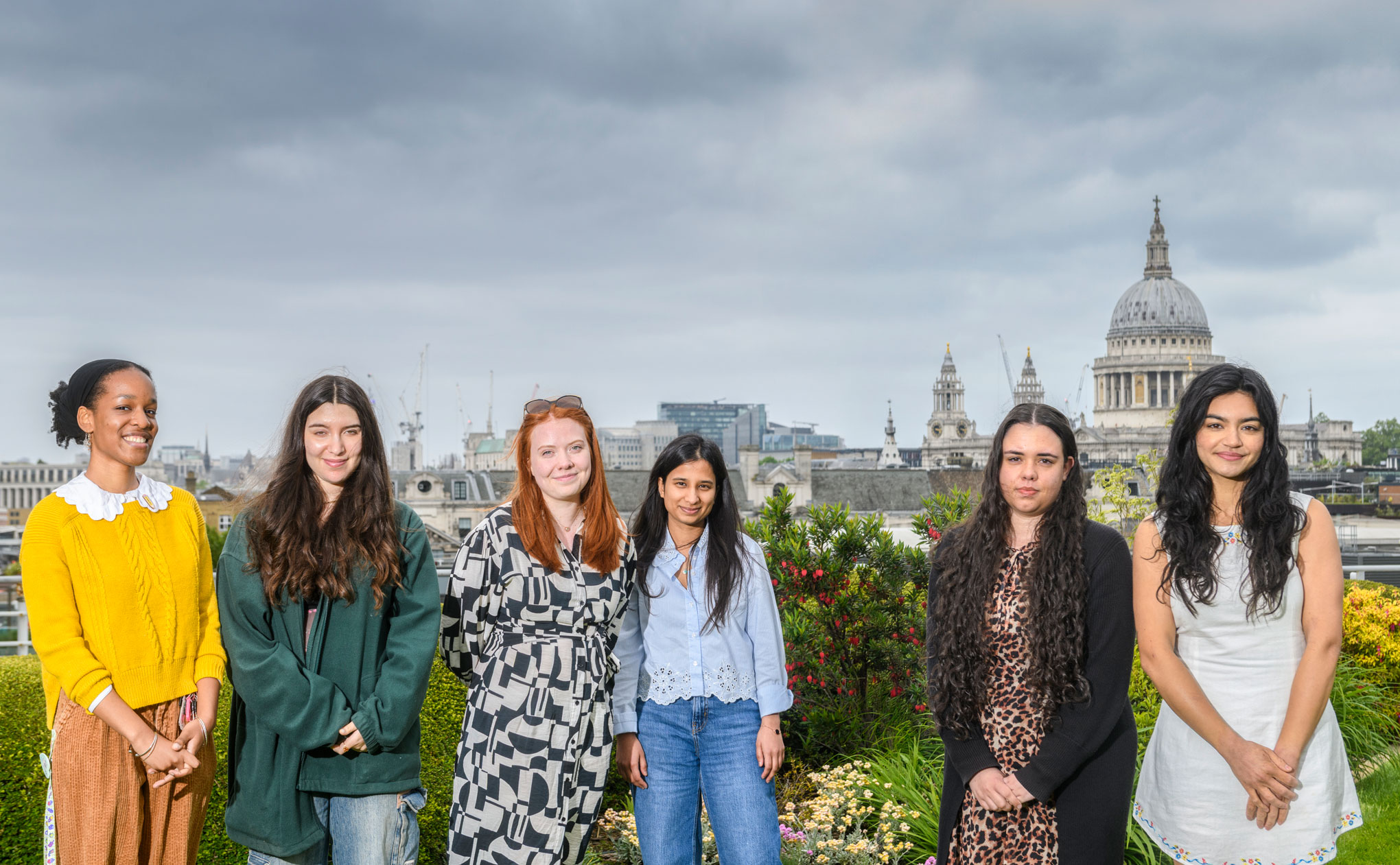 A group of young people photographed on an office rooftop garden with St Pauls and the skyline of London in the background.