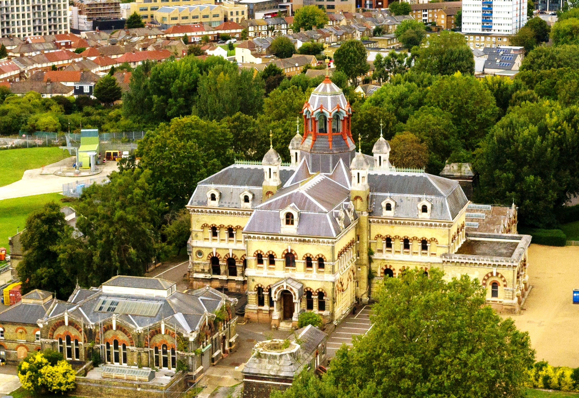 An elaborate gothic style brick and stone building, built to a cross plan, with a mansard roof and central cupola.