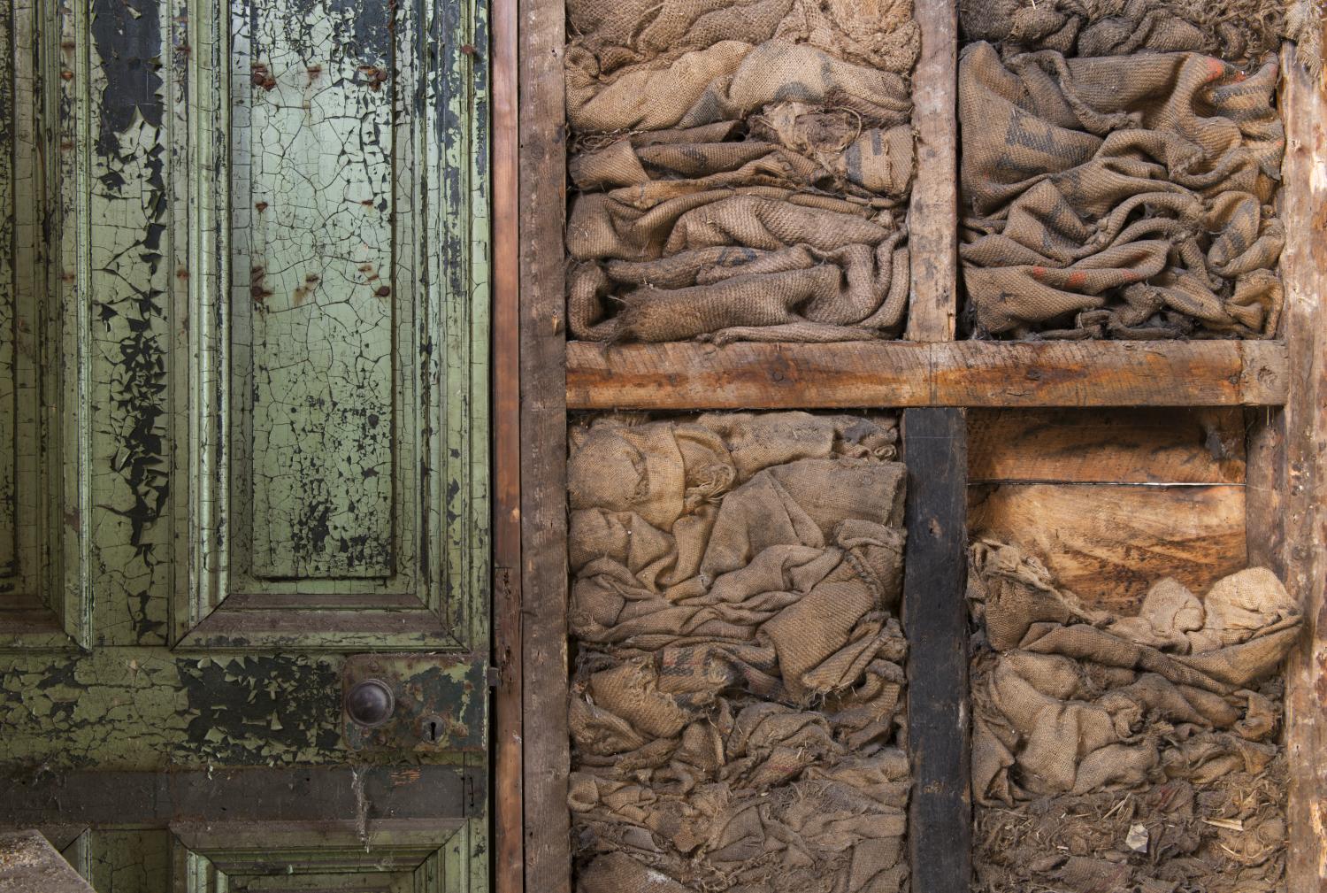 An open partition wall showing sacks used as insulation, with an old green door to the left.