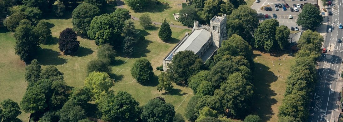 The Priory Church of St Peter is shown in an aerial view, surrounded by trees and with the landscaped Priory grounds around it.