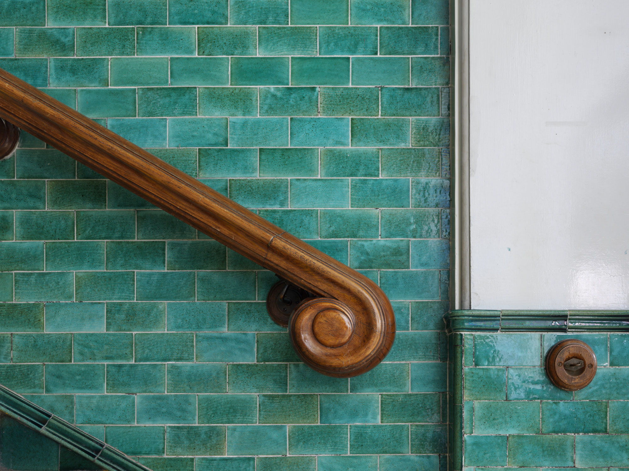 Curved wooden banister on a turquoise tiled wall.