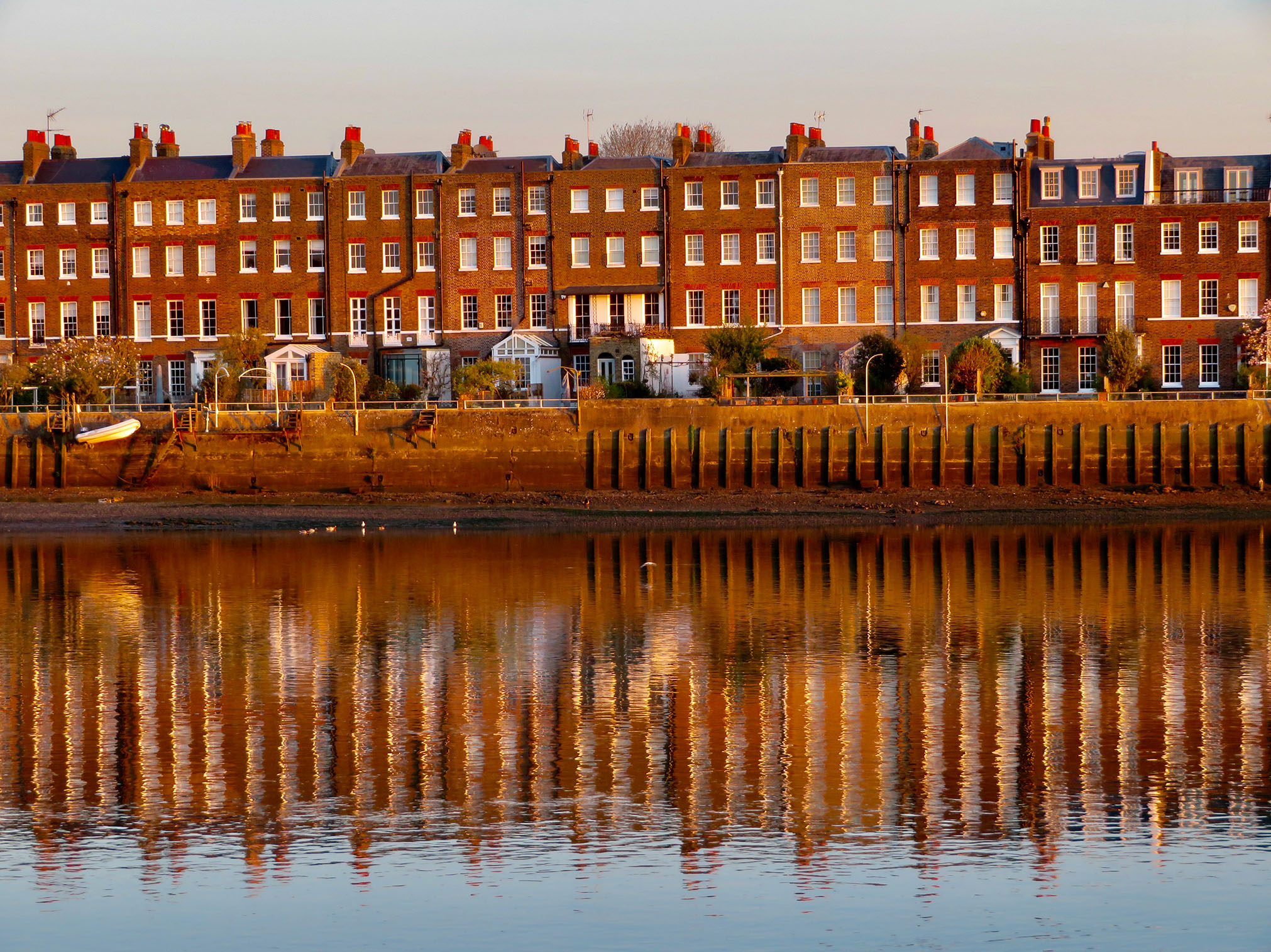 View of Hammersmith Terrace, a row of brick terraced houses along a riverbank reflected in the water.