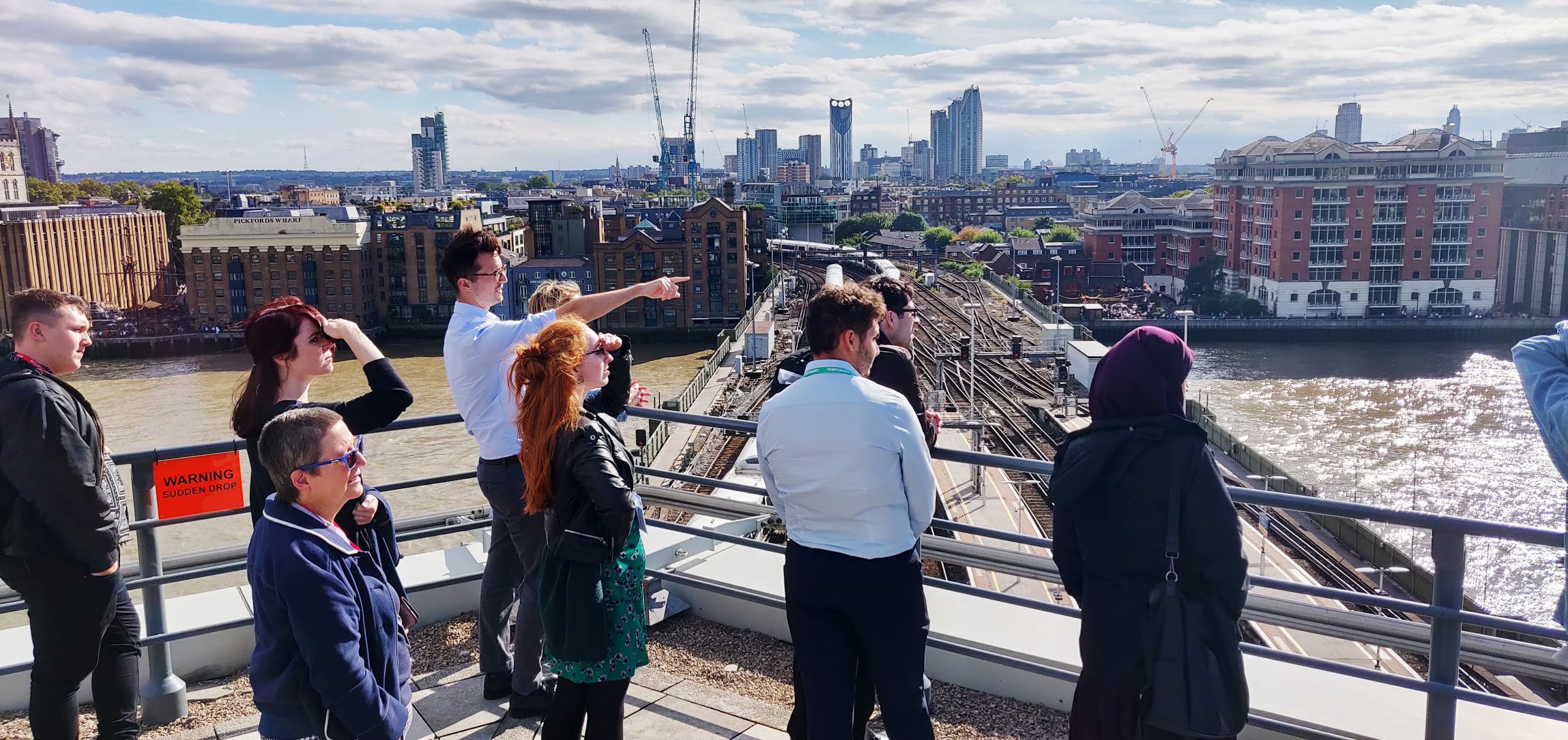 People looking across the Thames from a viewing point on top of a building.