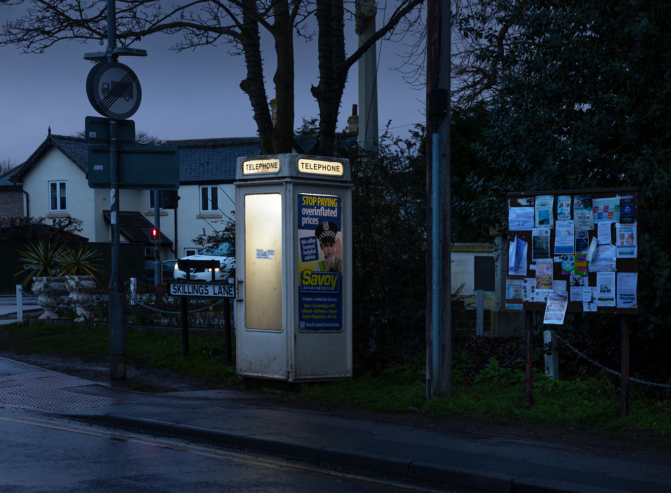 A pale plastic phone booth with posters and tickers shines on a dark street. 