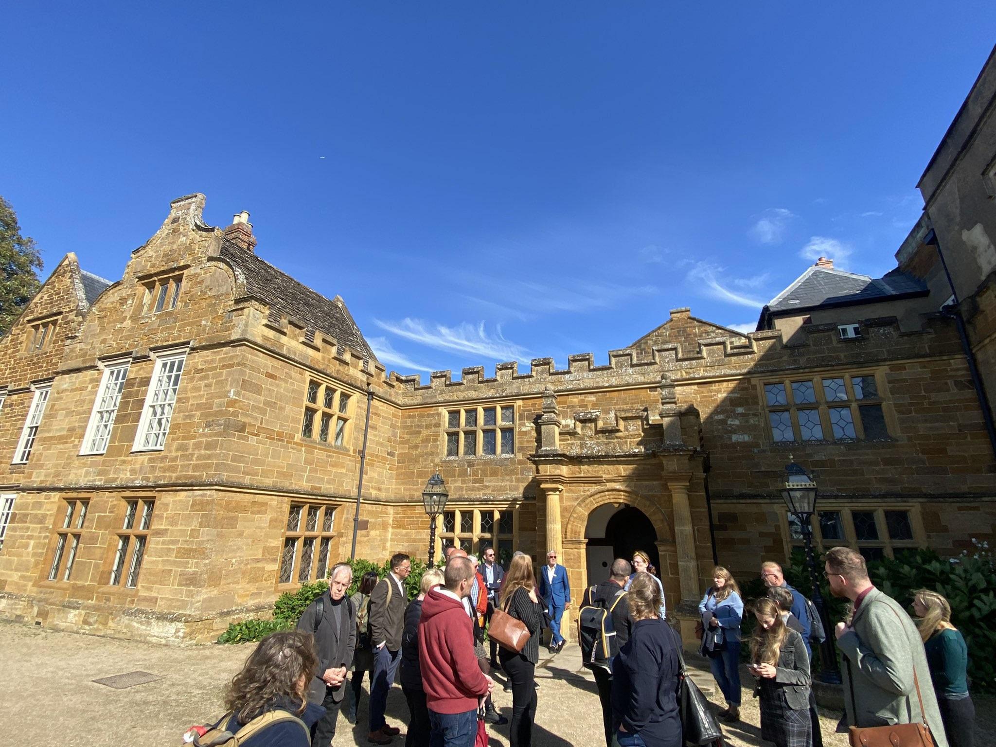 A group of people outside the entrance to a former abbey building built of mellow honey-coloured stone.