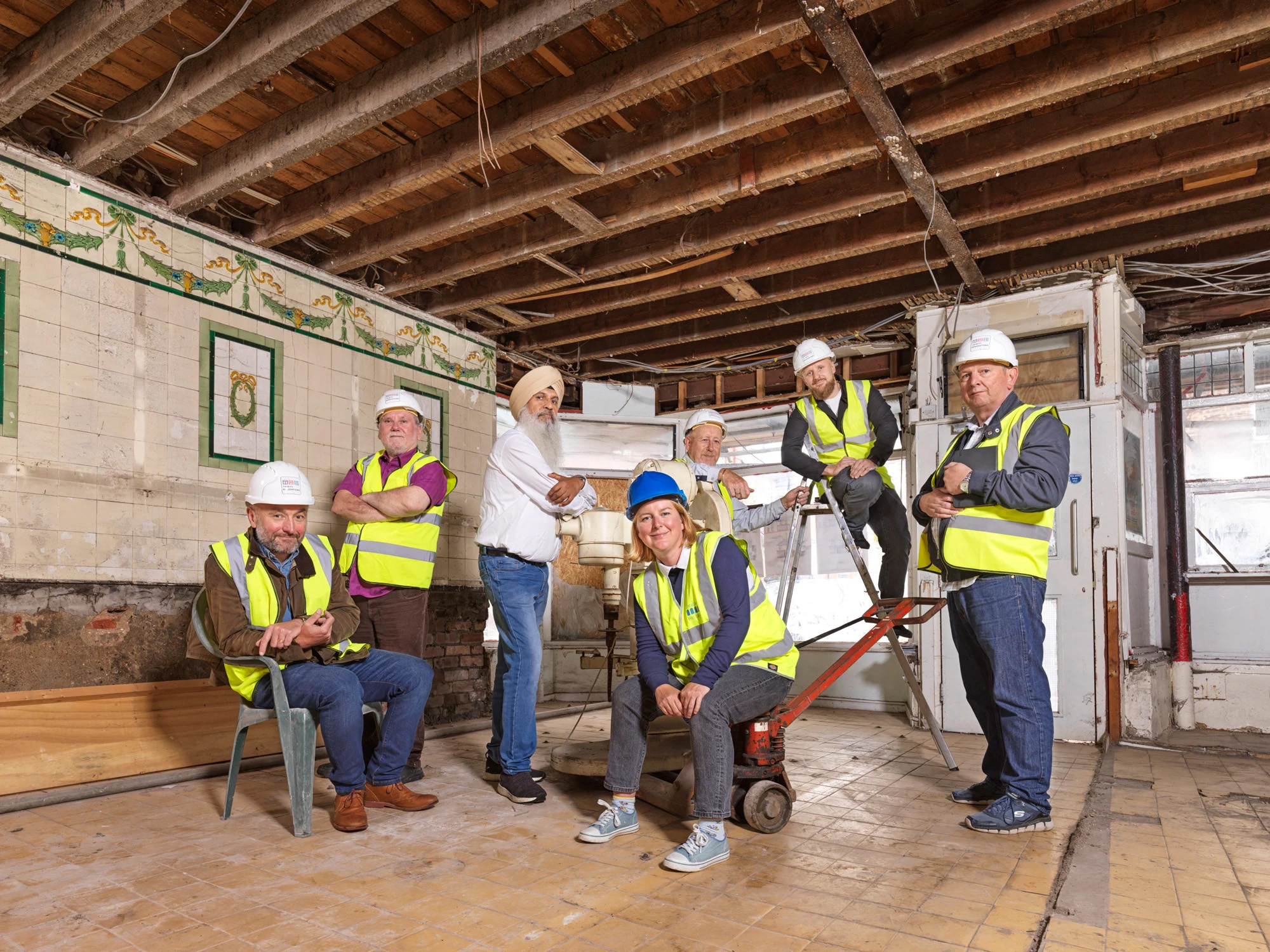 Colour photo of a group of 7 community group members posing for a group portrait at a construction site.
