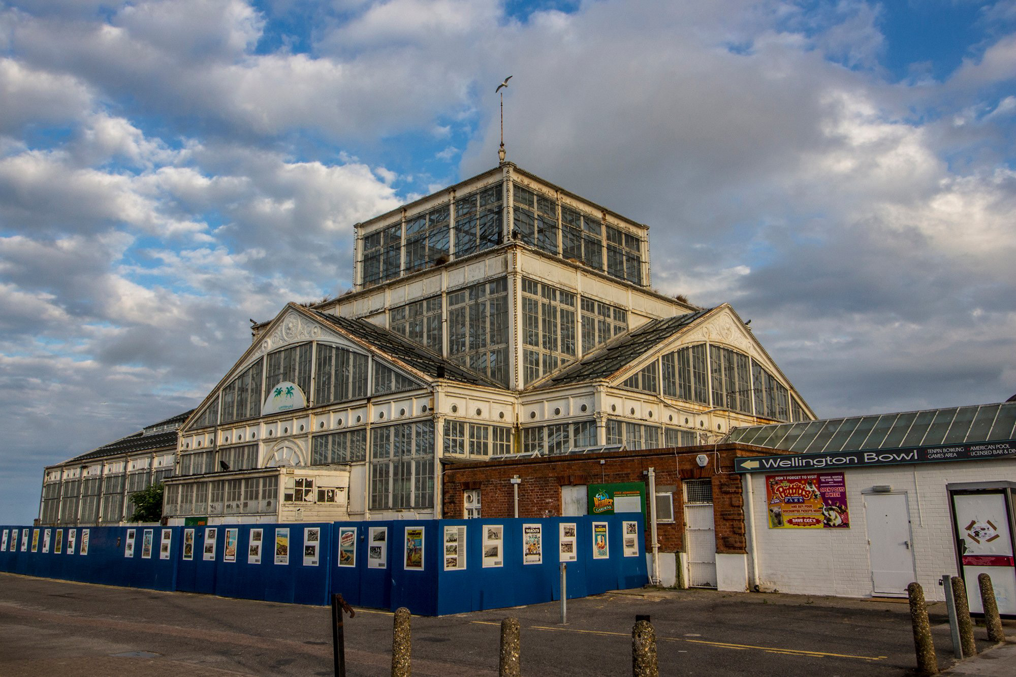 A large wrought iron and glass structure surrounded by hoarding boards