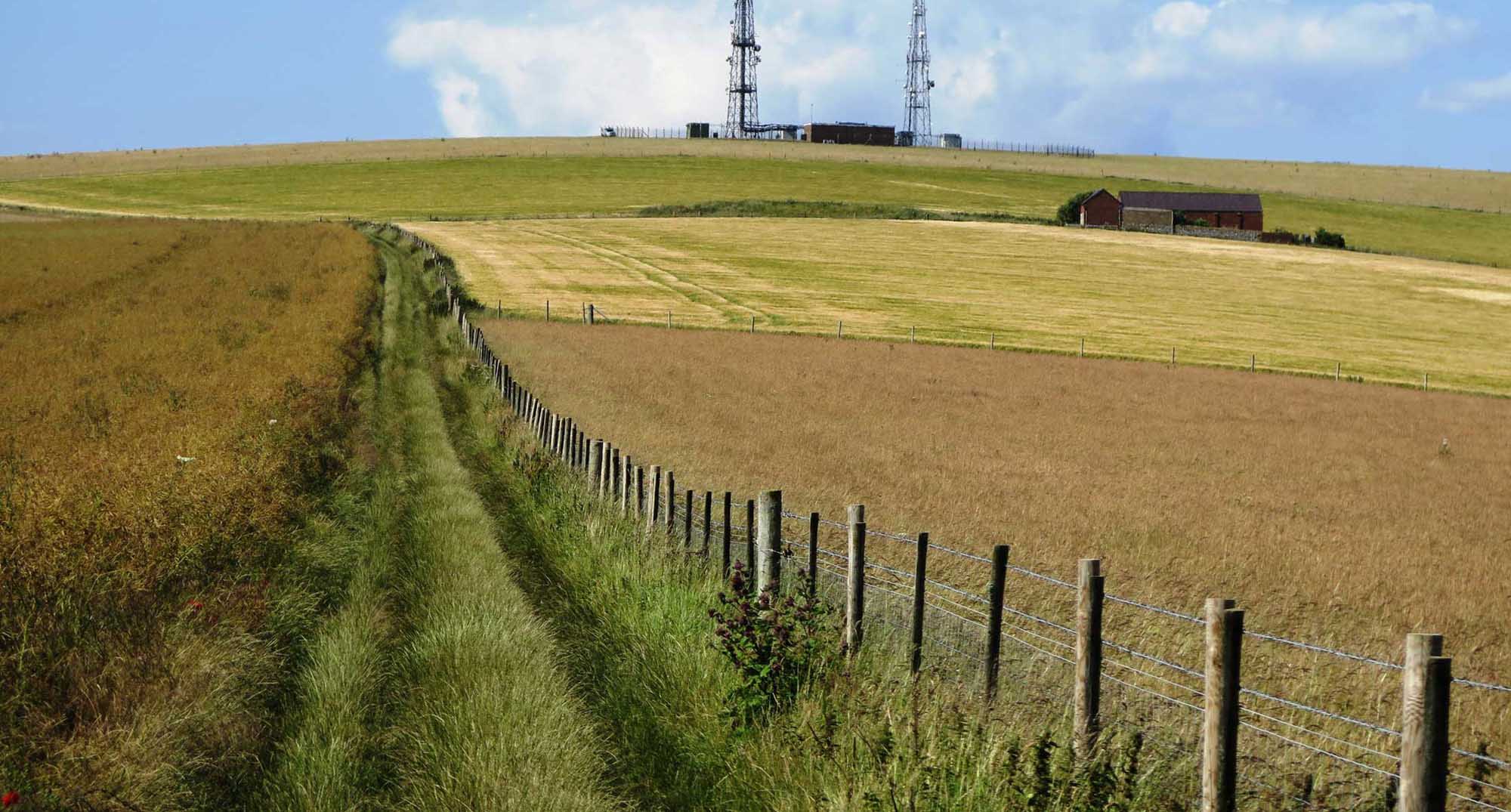 A landscape with fields, farm buildings and telecommunications masts.