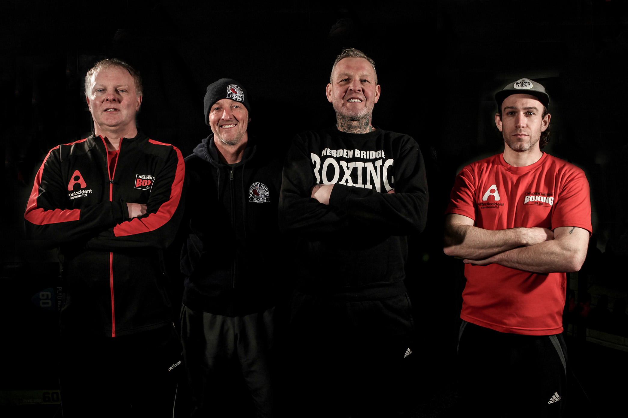 Portrait of four boxing coaches standing with arms crossed against a black background