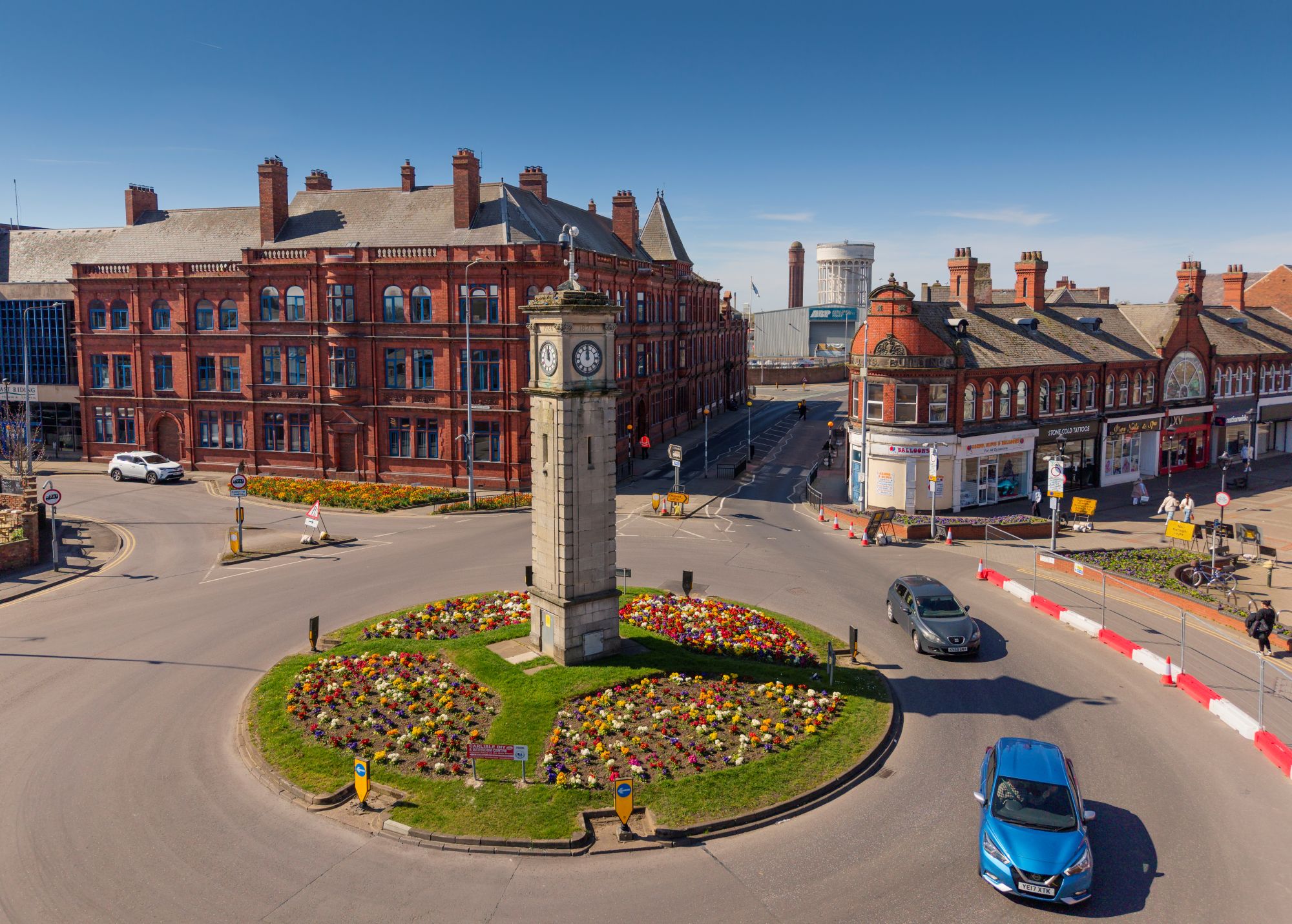 Photo of a street scene with a clock tower in the middle of a roundabout.